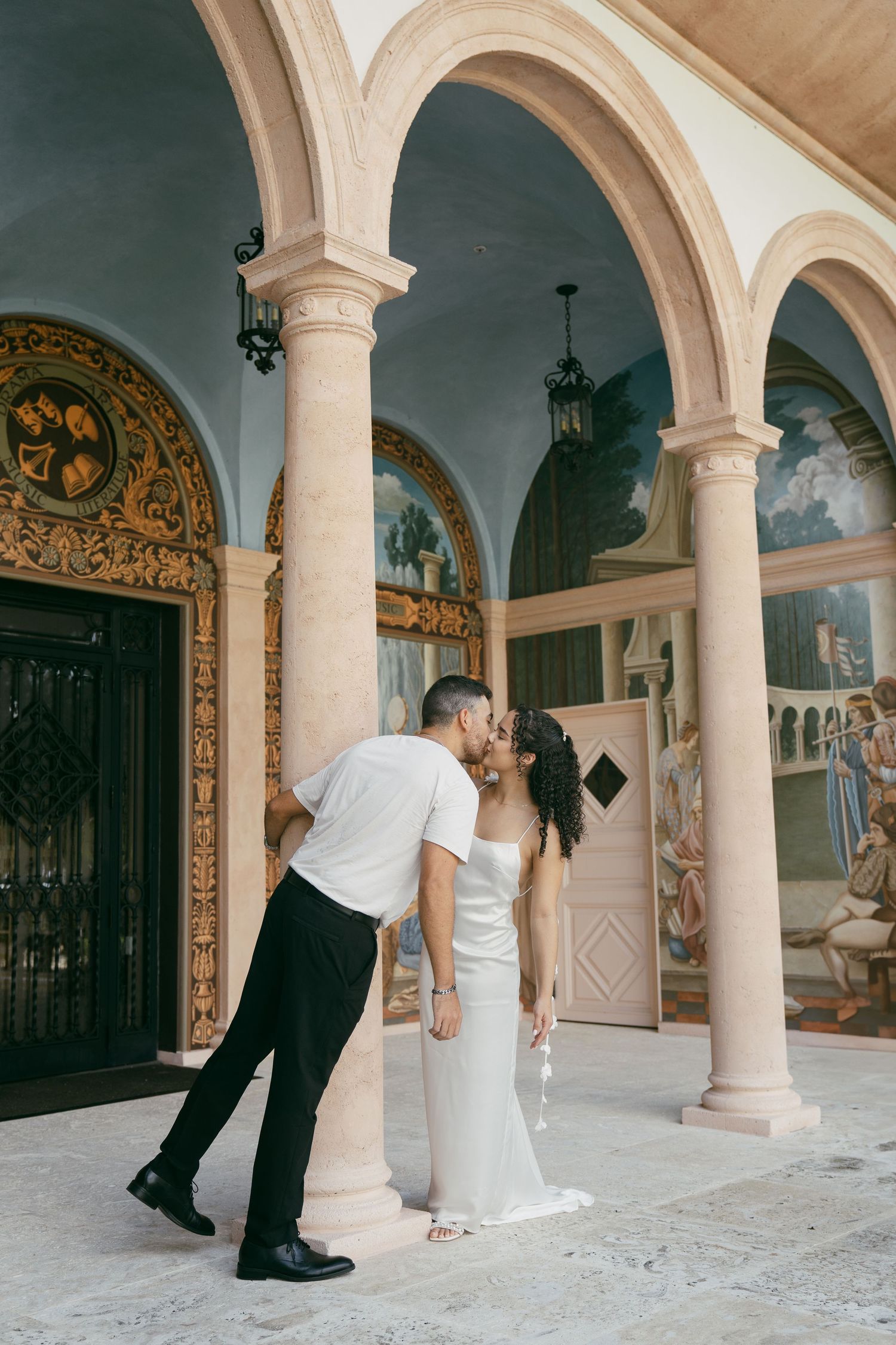 Couple performing dynamic dance sequence under classical stone archways with decorative details and murals.