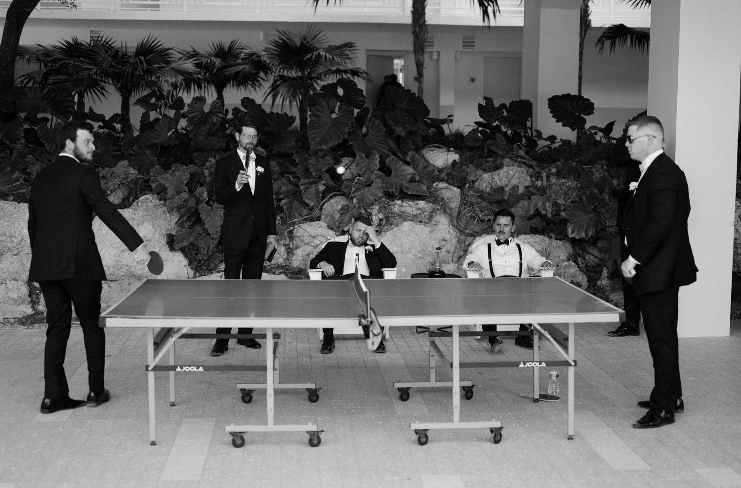 A vintage black and white photograph shows people playing table tennis on a portable ping pong table at an indoor venue.