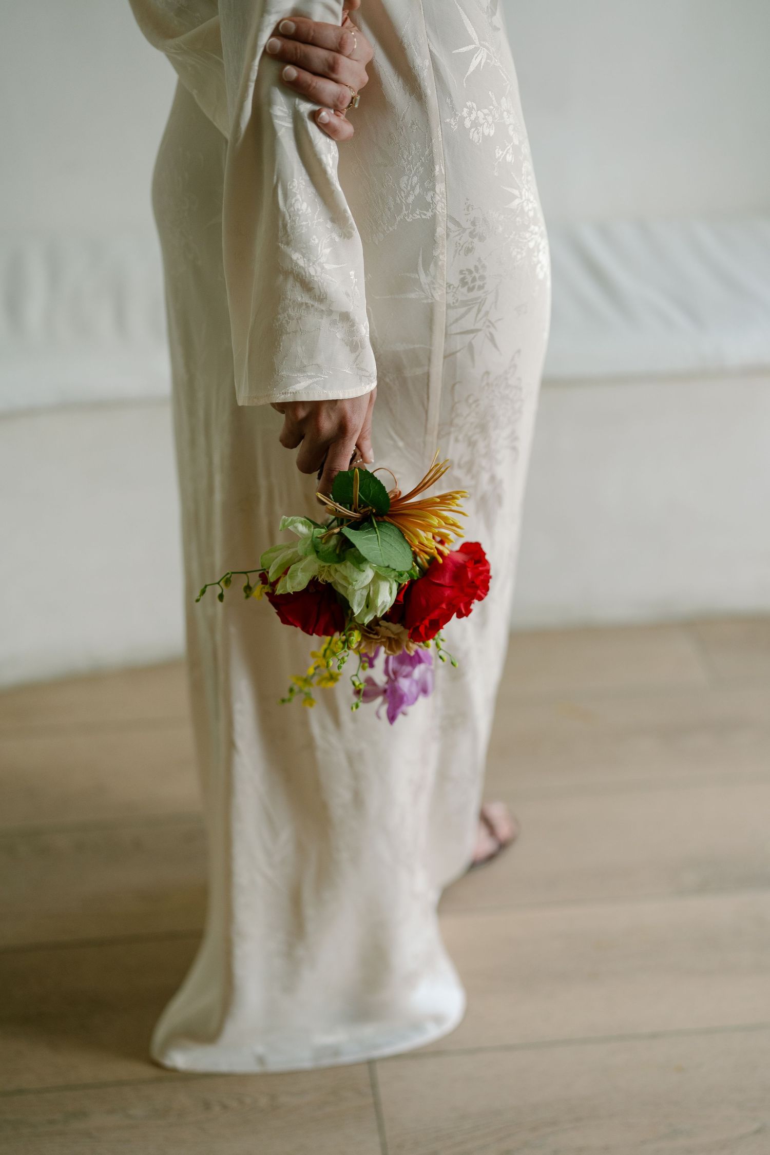 Elegant white wedding dress detail with colorful floral bouquet.