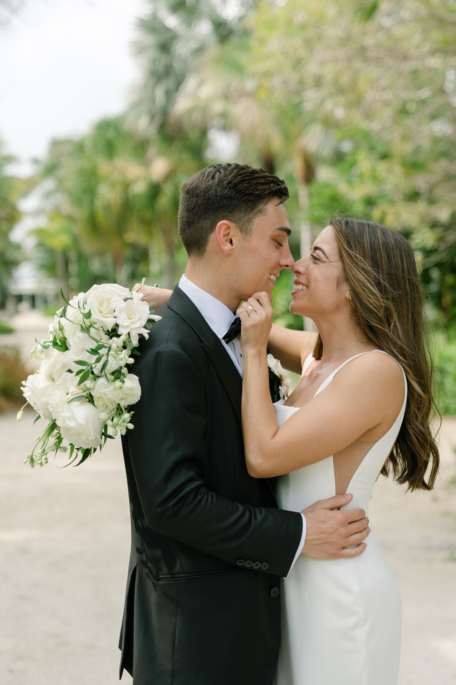 Bride and groom sharing a romantic moment, nearly kissing, surrounded by palm trees.