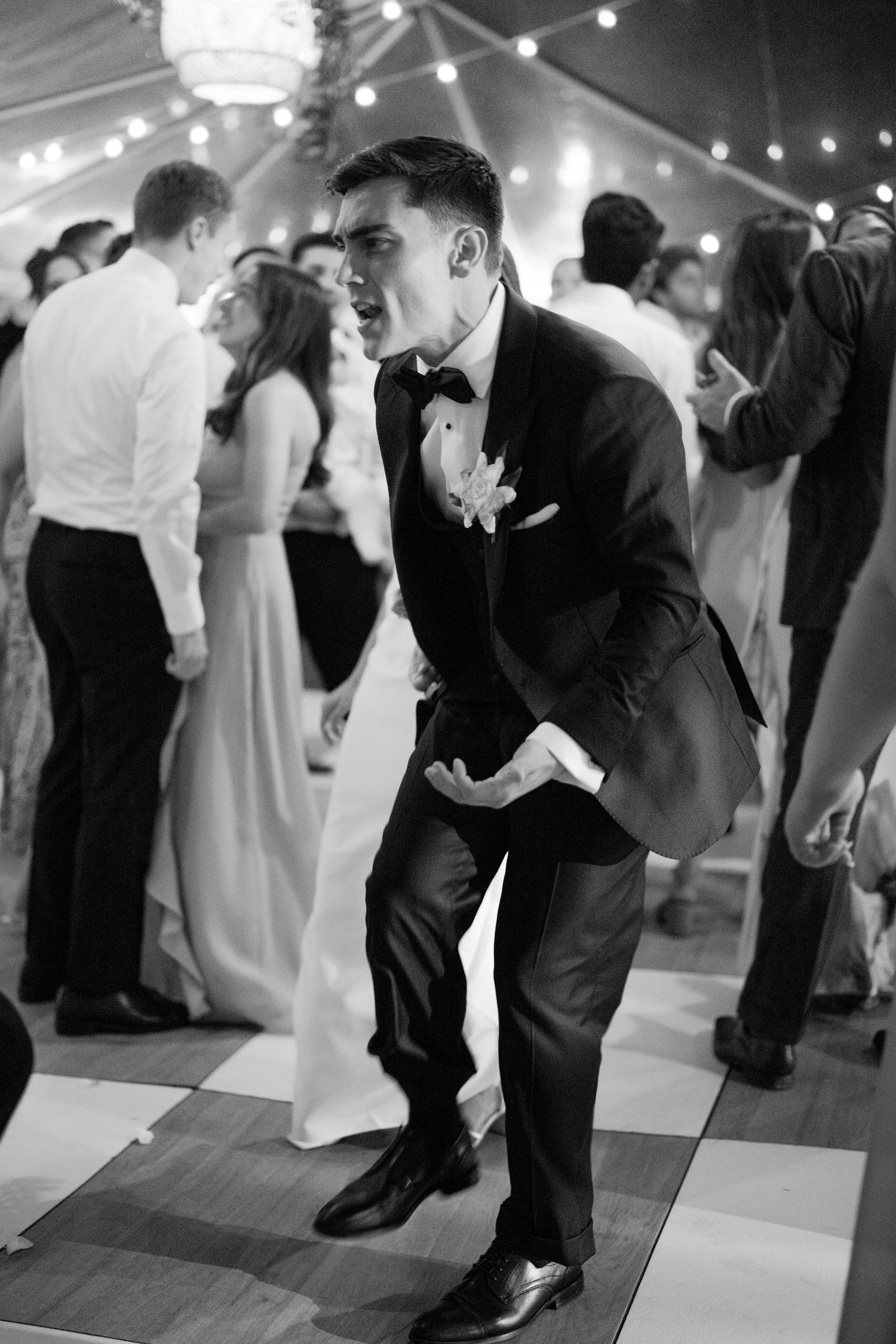 Black and white photo of groom in tuxedo dancing energetically on wedding reception dance floor.