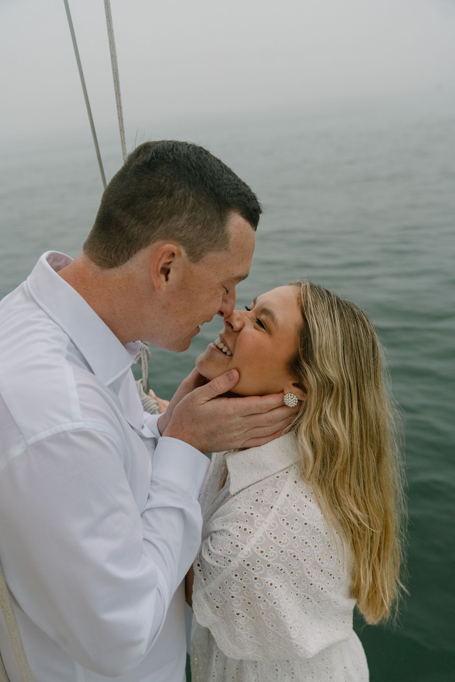 Romantic couple sharing an almost-kiss on a sailboat, man gently holding womans face, ocean visible behind them.