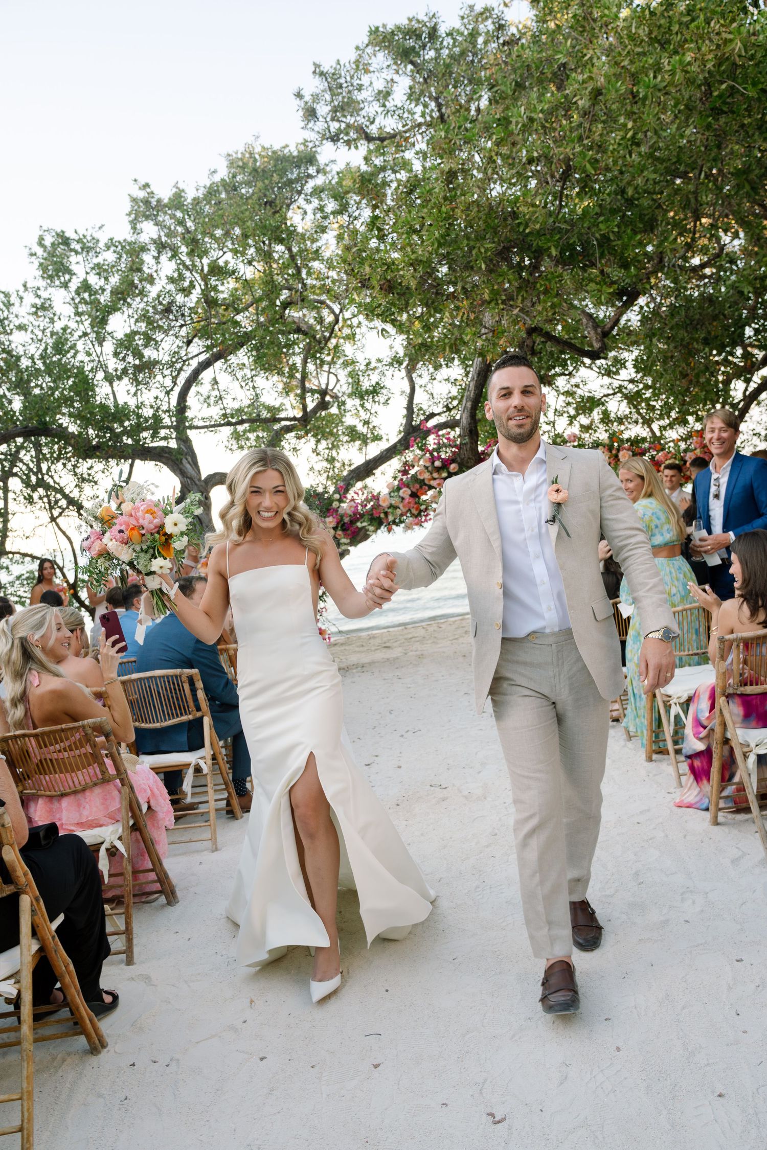 Wedding celebration on a sandy beach with guests in light summer attire.