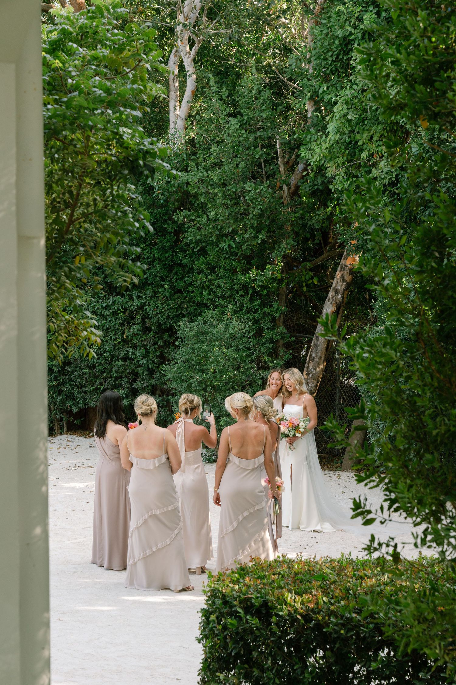 Bridal party walks together on a white sandy path surrounded by tropical greenery.