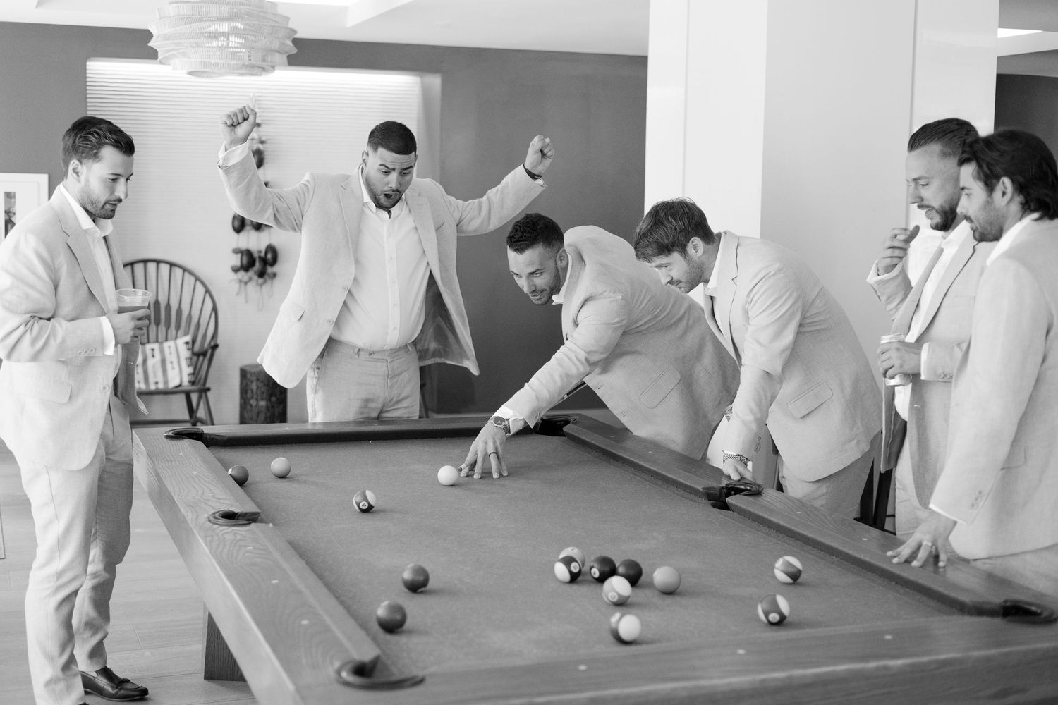 Black and white panorama of groomsmen playing pool in formal attire.