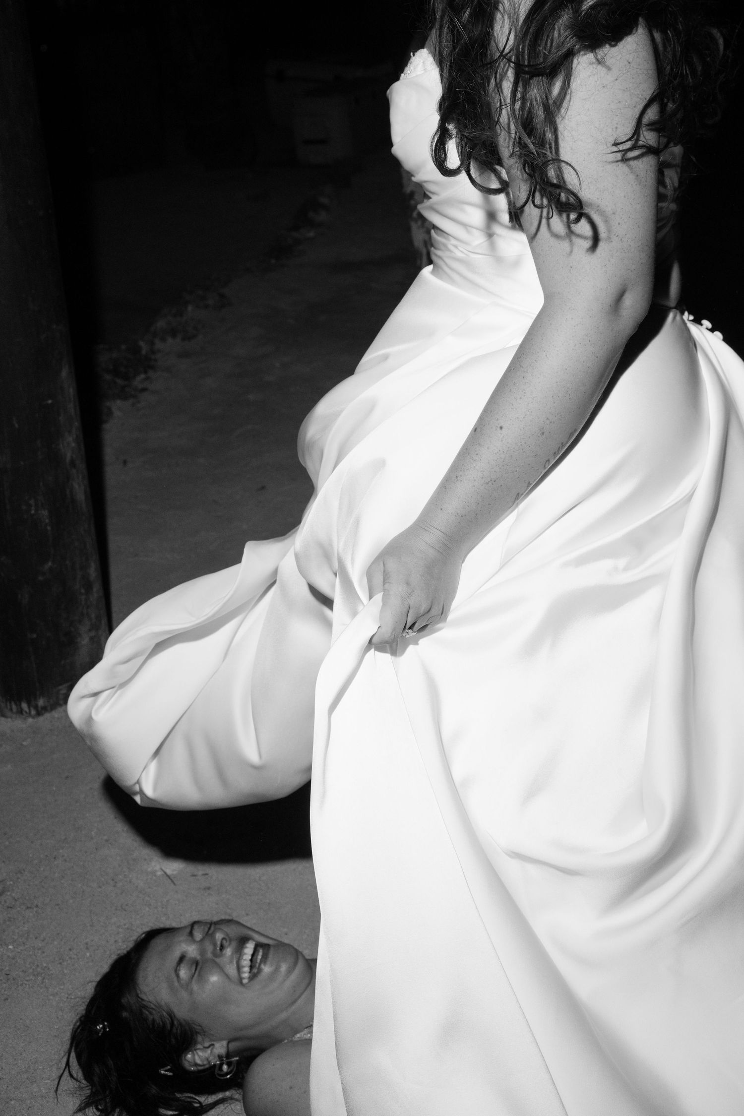 A black and white image shows a woman in a flowing white dress standing in a dimly lit room.