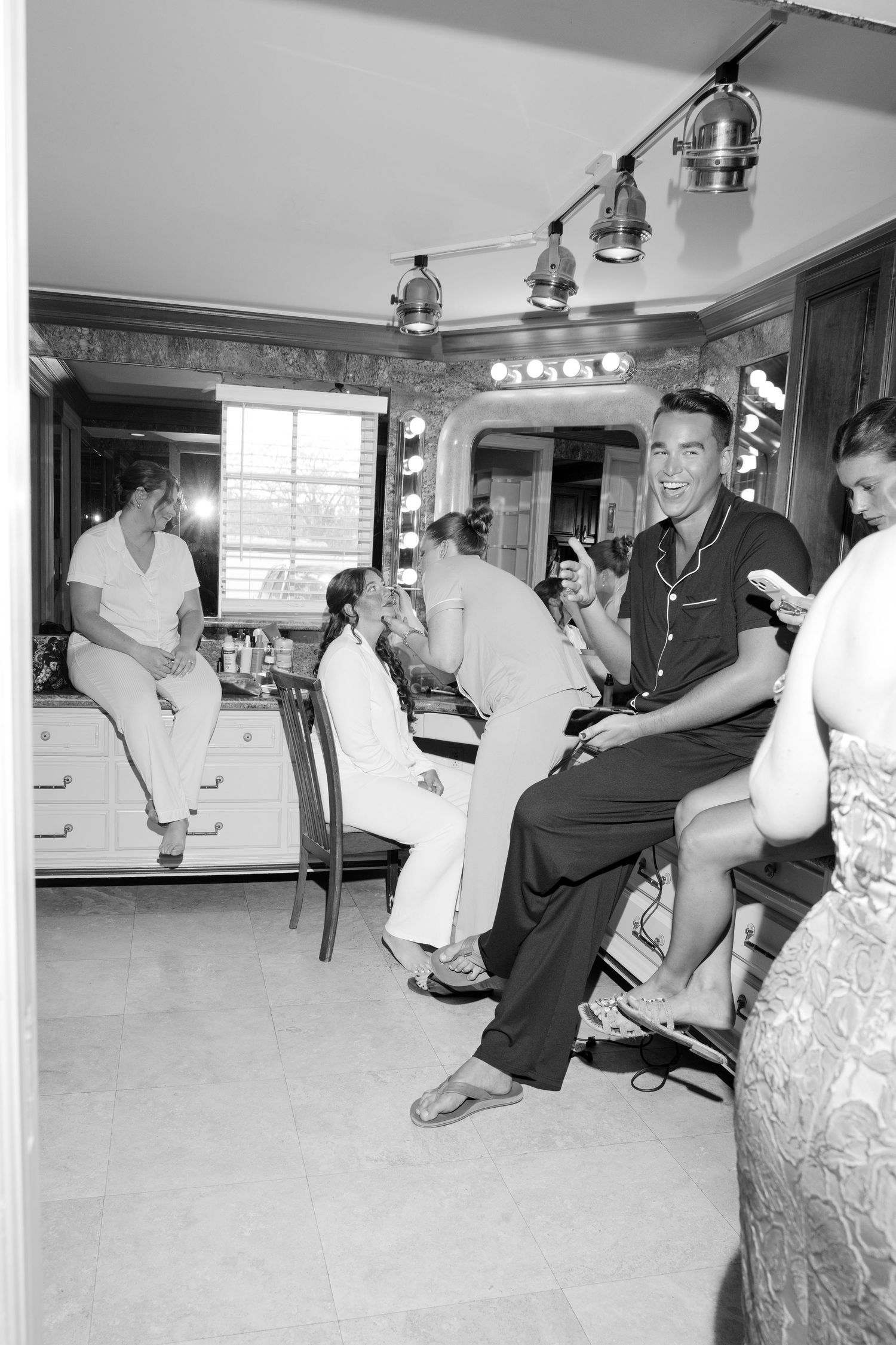 Vintage black and white photo of men relaxing in a dressing room with vanity mirrors and bright lights.