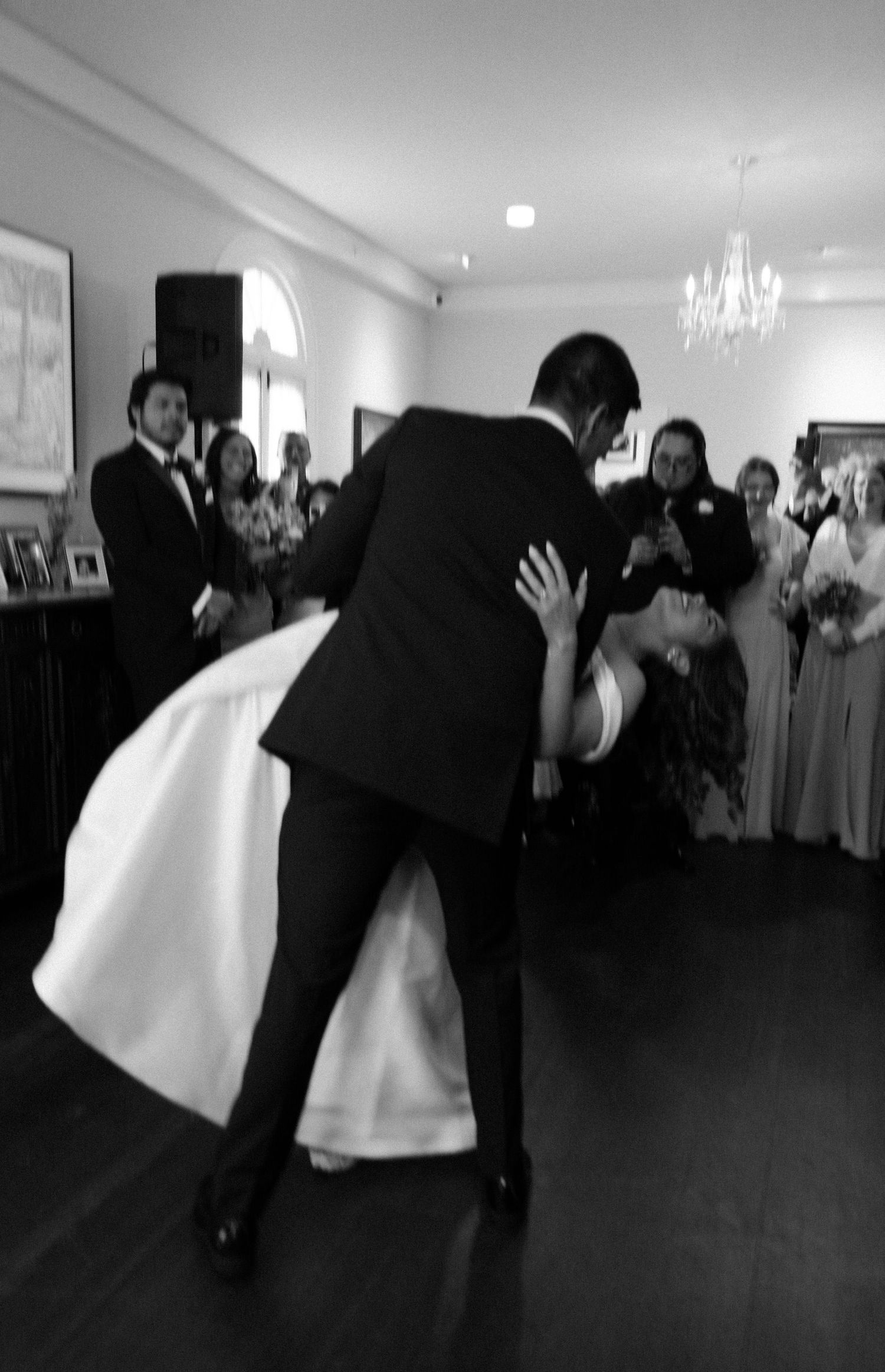 A couple shares a romantic dance dip at a wedding reception while guests look on in black and white photography.
