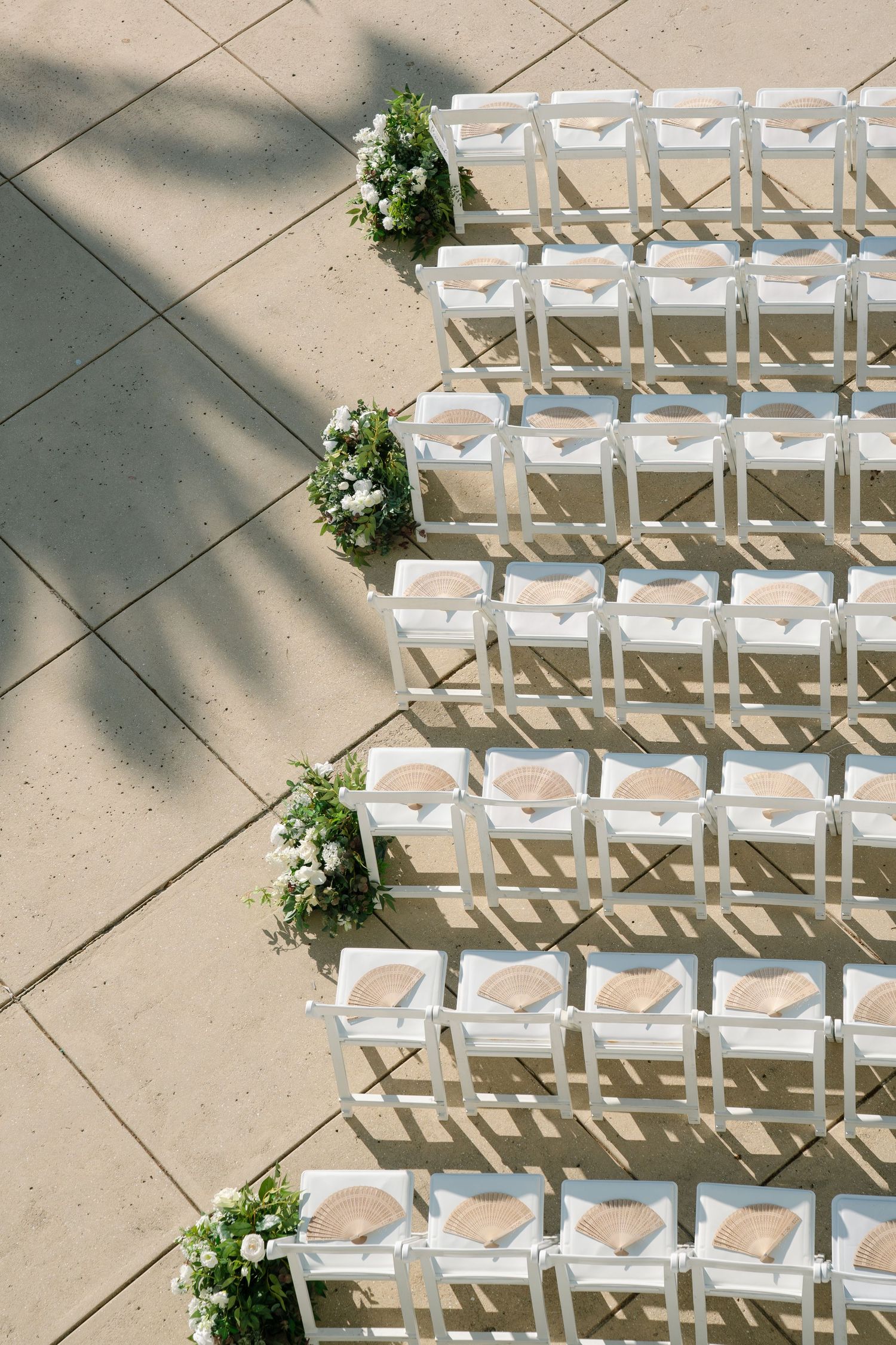 Rows of white wedding ceremony chairs arranged outdoors with floral arrangements marking the aisle ends.