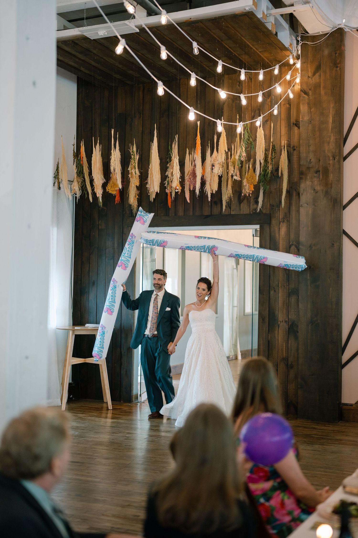 Wedding celebration in a rustic venue with string lights and decorative banners.