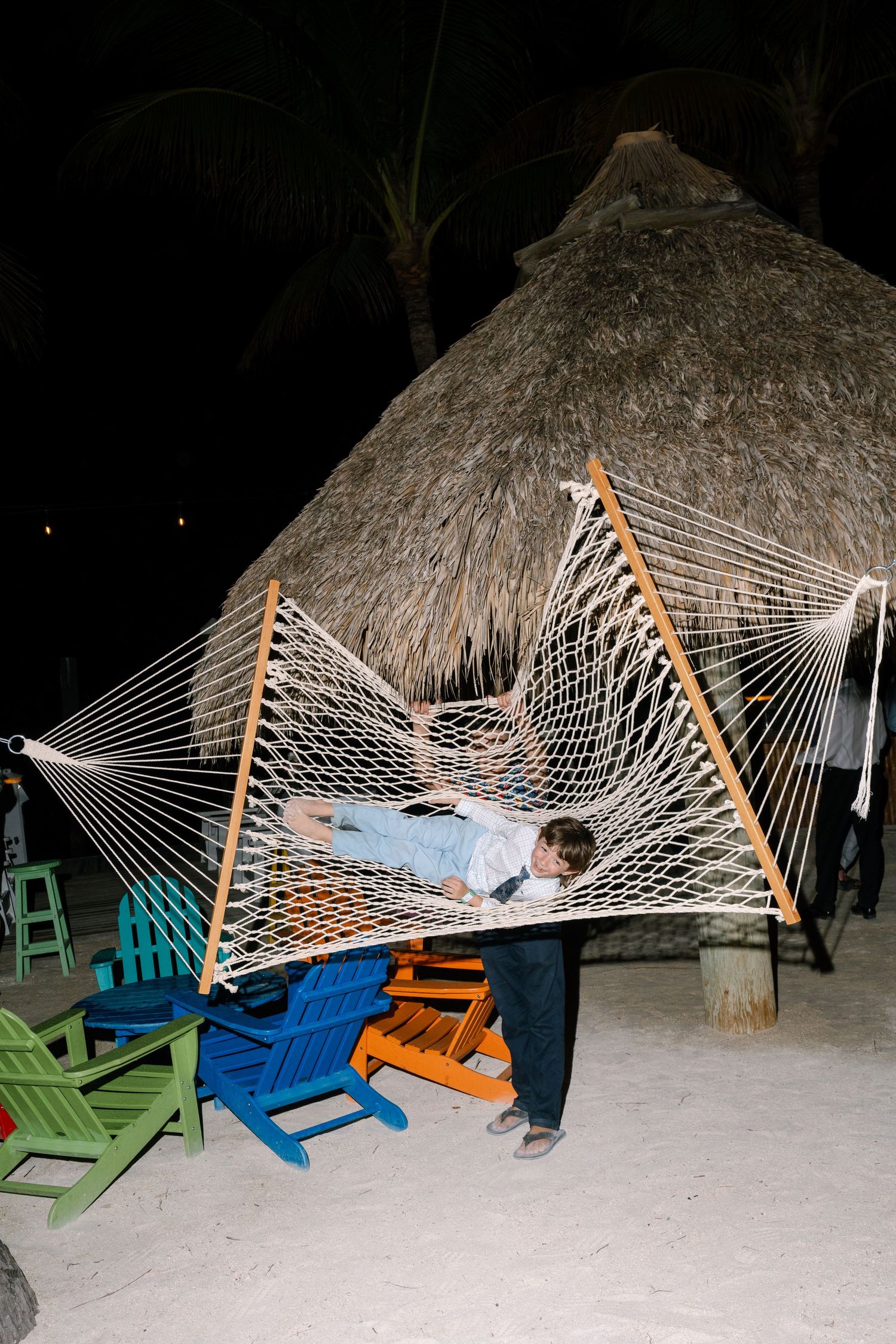 An image of a person relaxing in a hammock at night, surrounded by a thatched-roof structure.