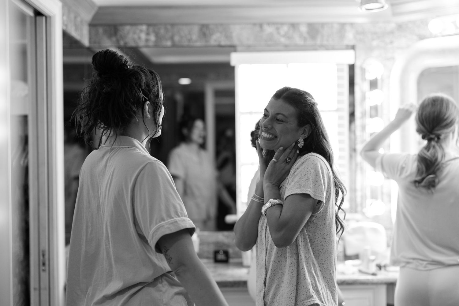 Two women share a joyful moment in a bright room, one touching her face while smiling in a black and white photo.