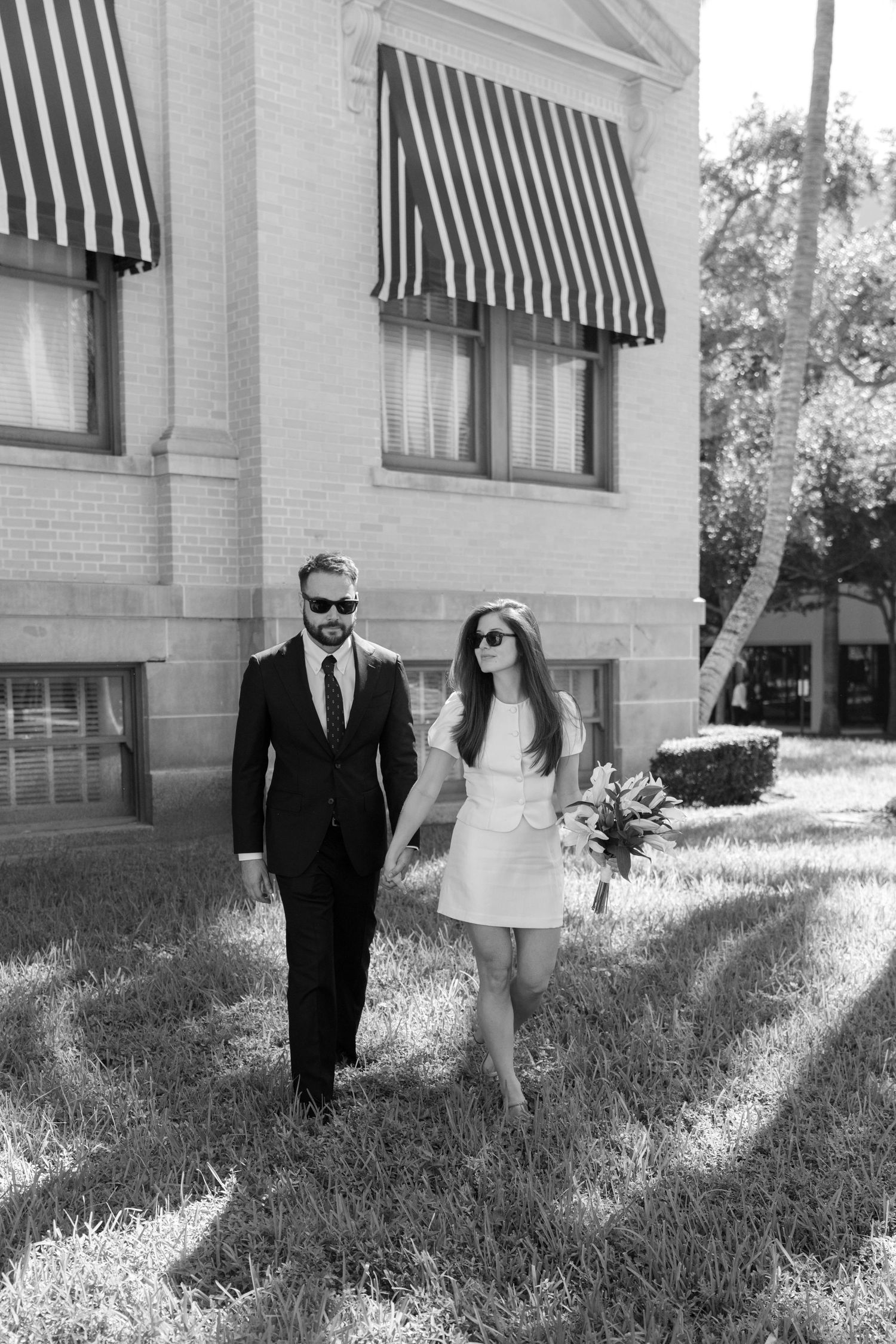 Black and white photo series of a couple walking together on grass near a building with striped awnings.