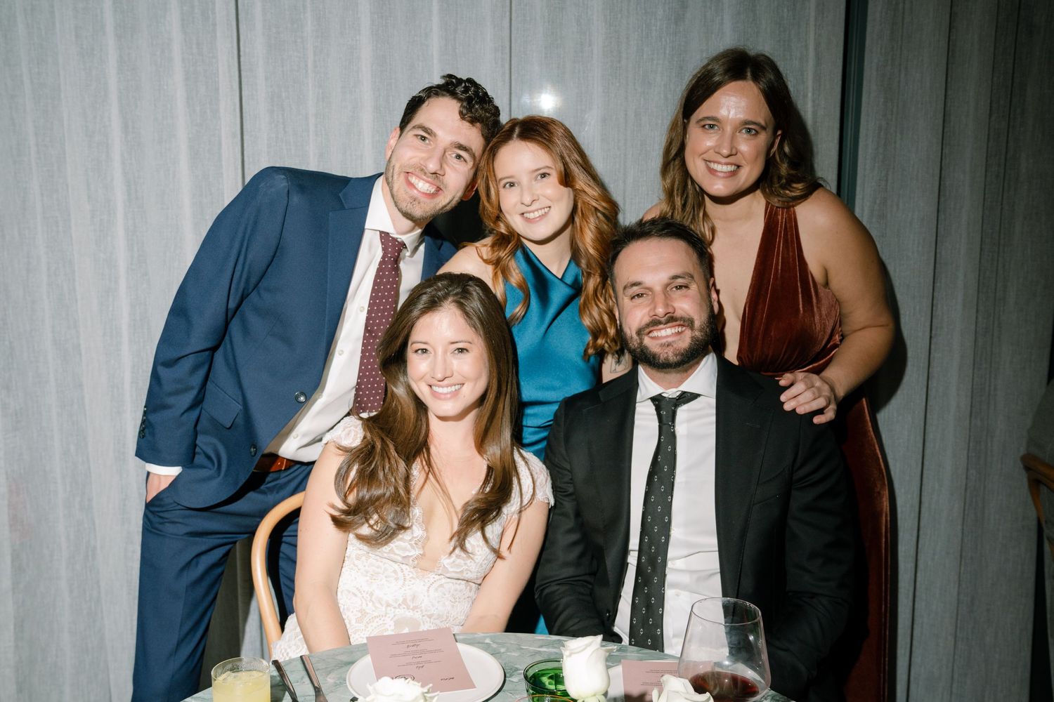 A group of wedding guests pose together at a formal reception table.