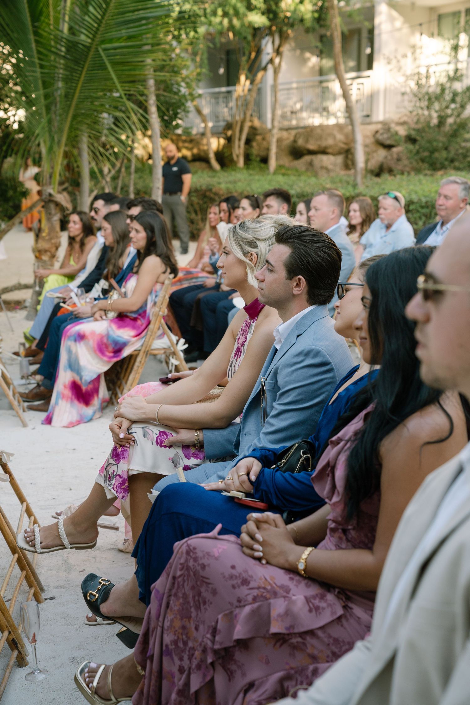 Wedding guests seated in wooden chairs watching an outdoor ceremony.