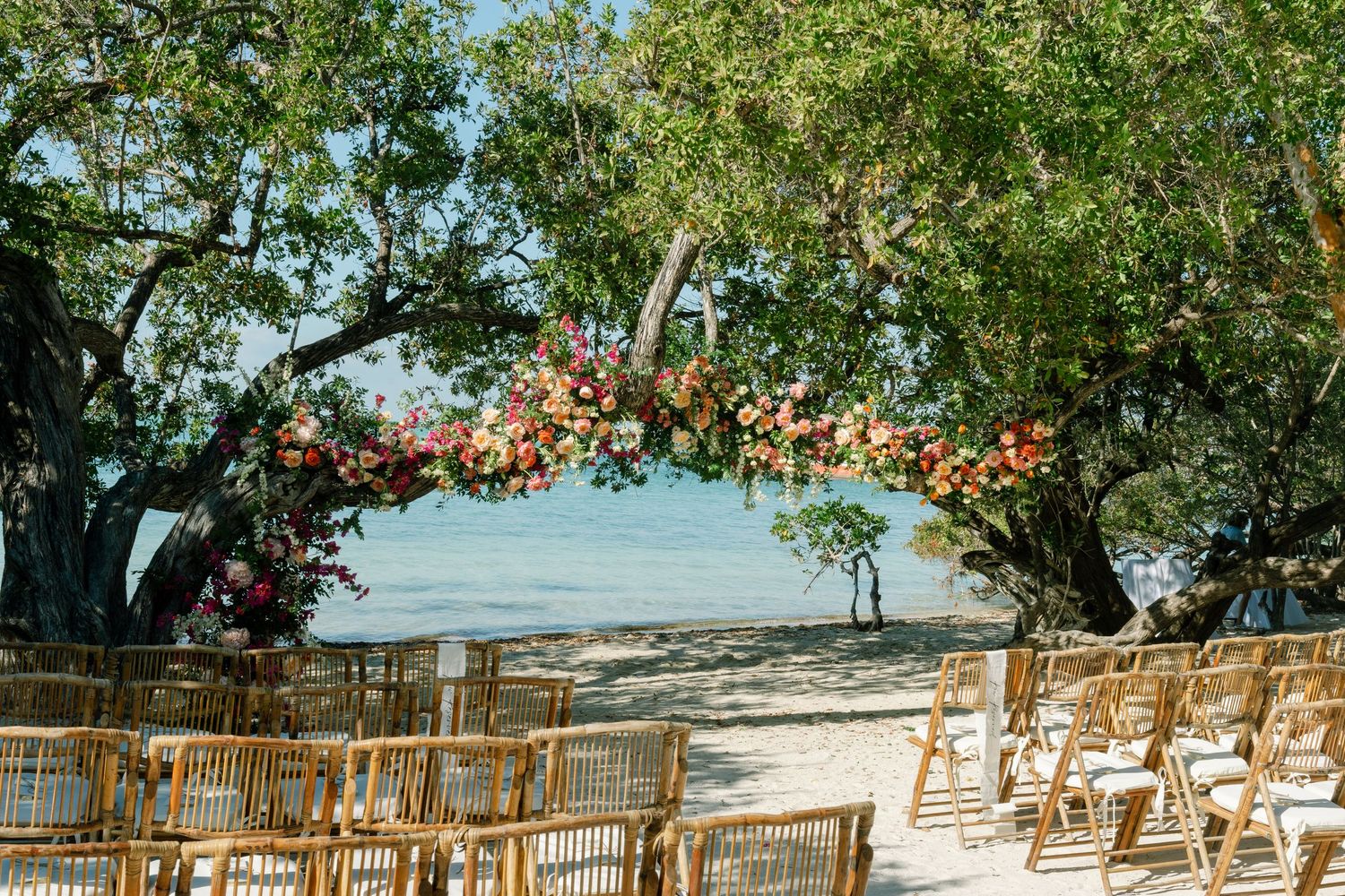 A panoramic view of wooden chairs arranged on a beach for a tropical destination wedding ceremony with ocean backdrop.