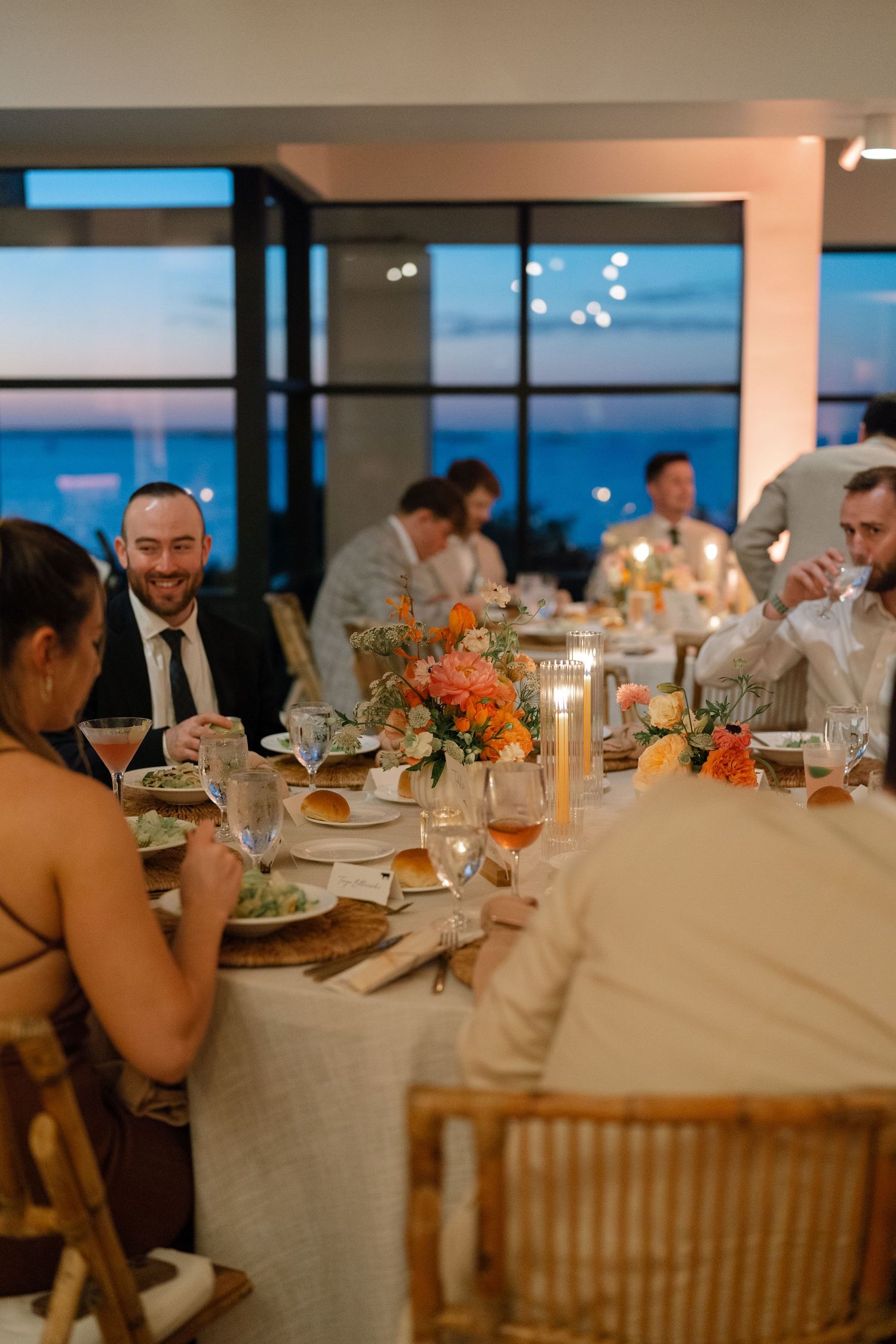 Wedding reception dinner tables set with elegant floral centerpieces and glowing candles at sunset.