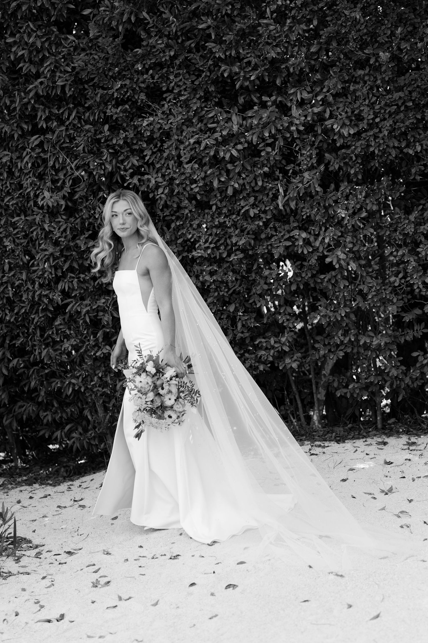 Artistic black and white bridal portraits showing flowing veil and dress against dark foliage.