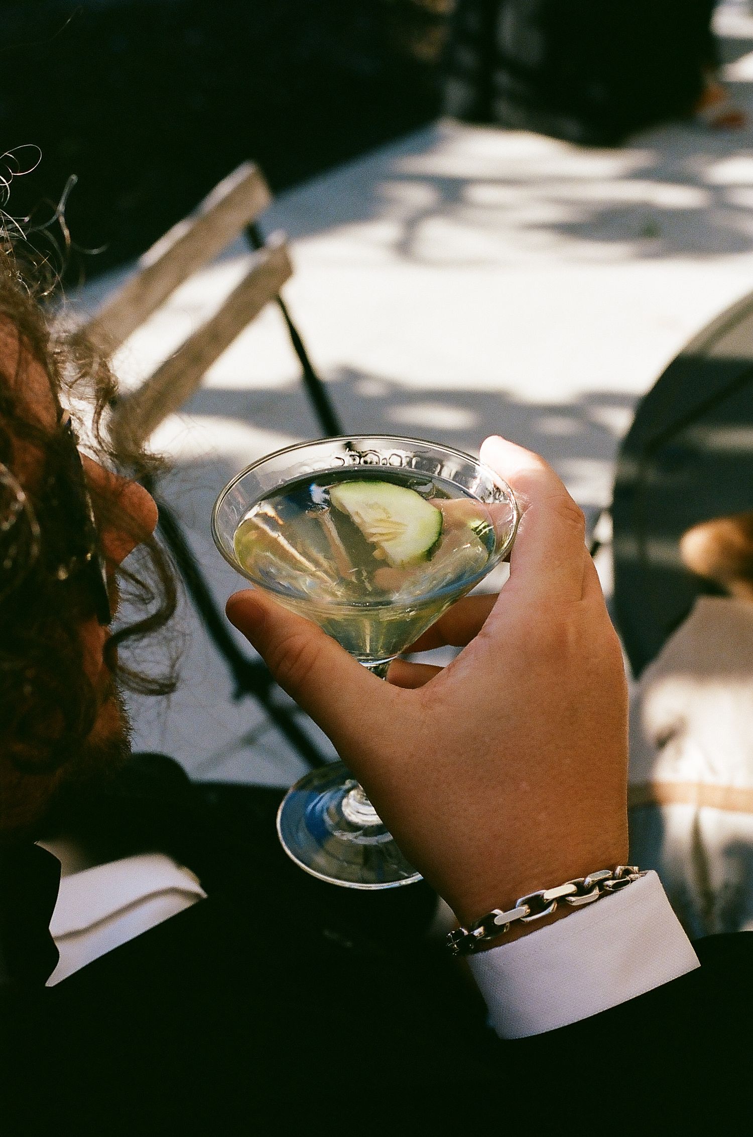 Hand holding a martini glass with clear liquid and garnish at a dimly lit bar setting.