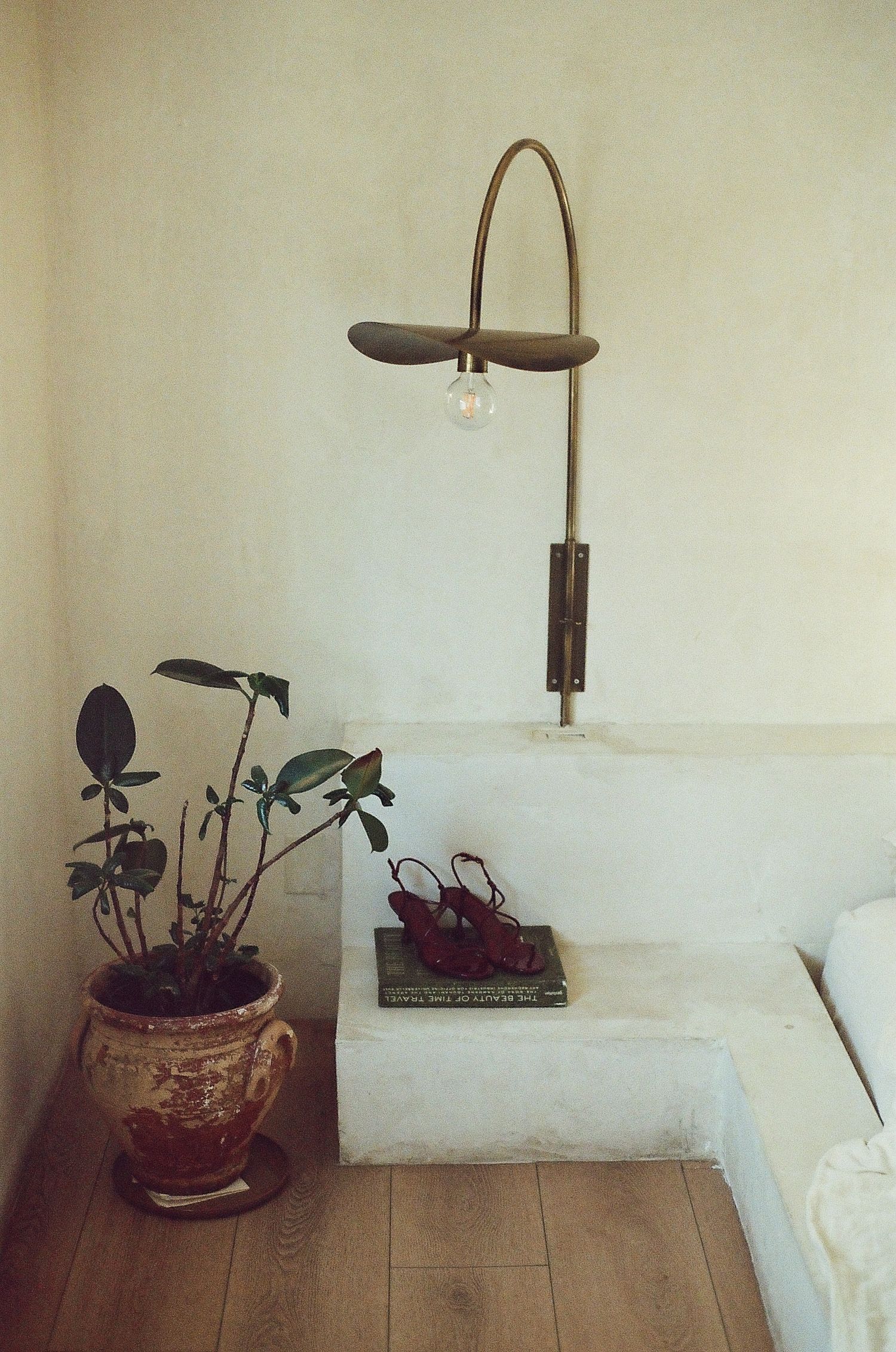 Minimalist bedroom interior with white bedding, wall lamp, and potted plants on bedside table.