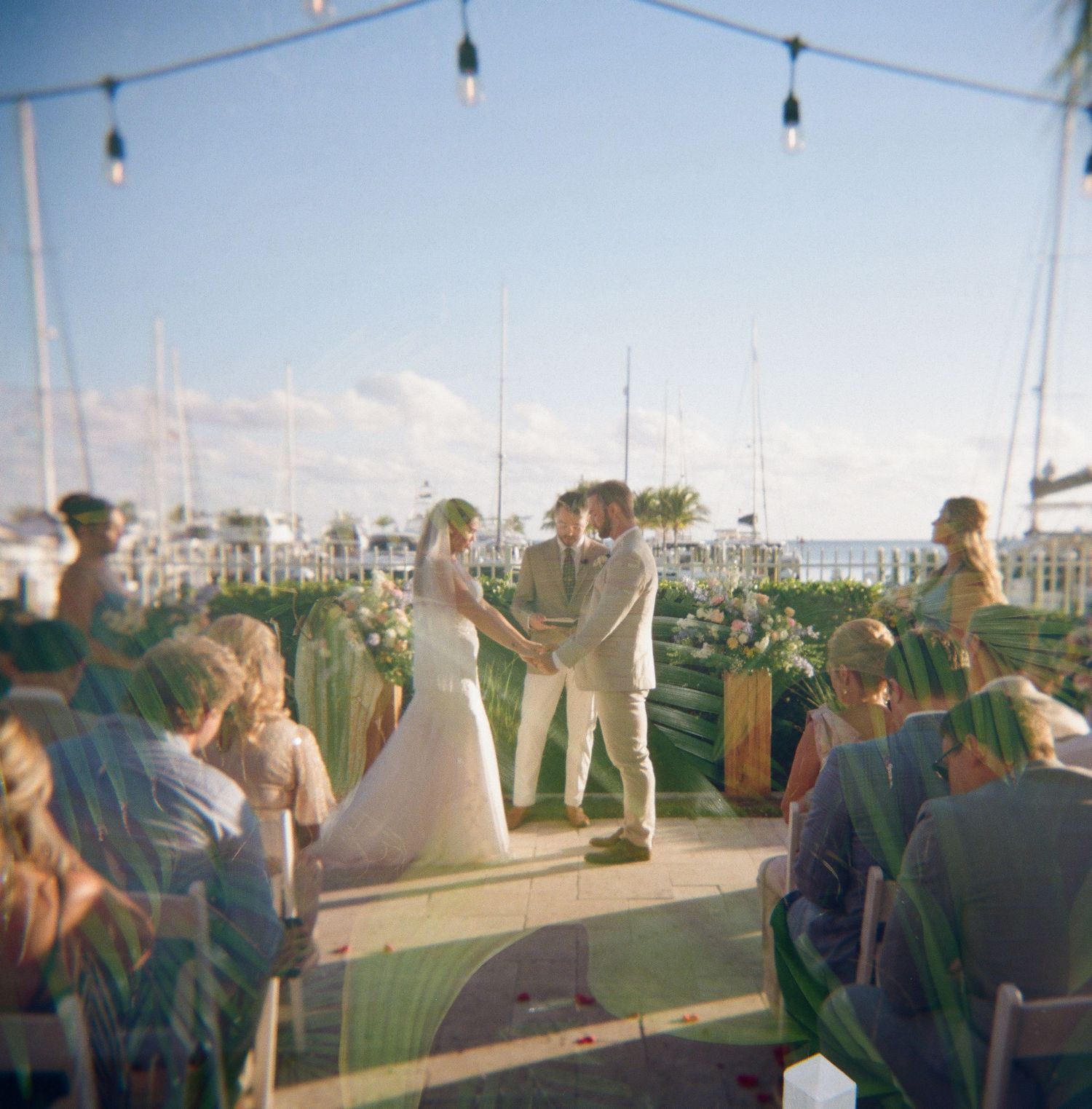 Outdoor wedding ceremony setup with string lights and ocean view in the background.