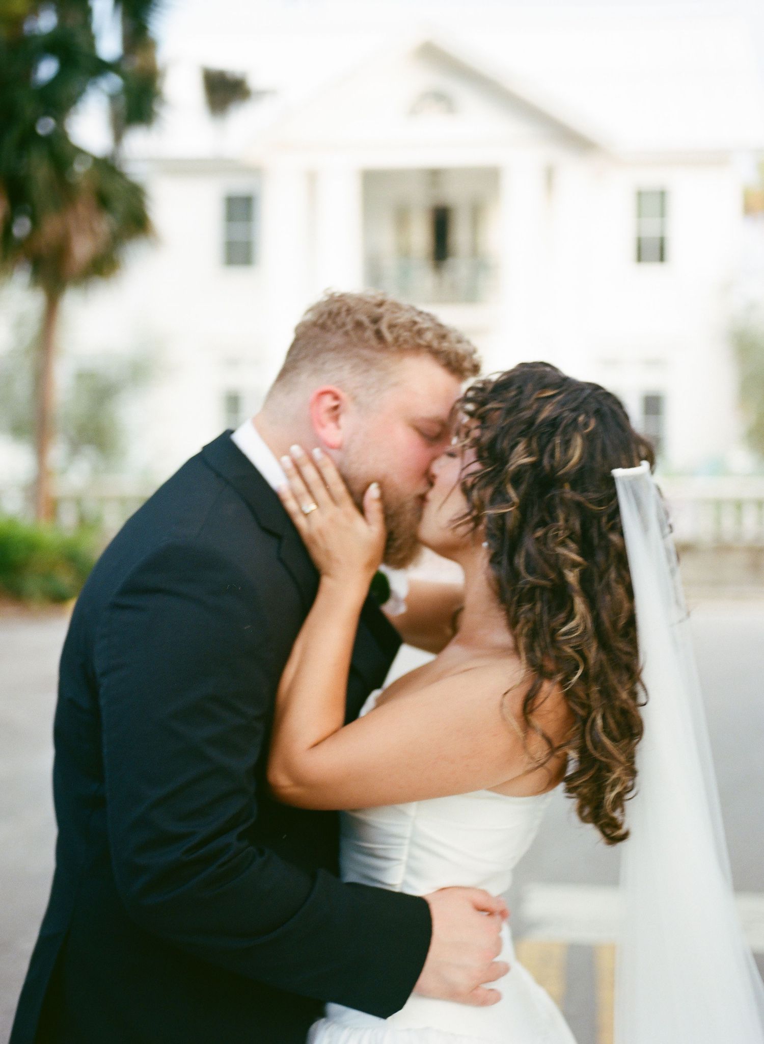 A romantic wedding couple shares intimate kisses in a series of photos with white buildings in the background.