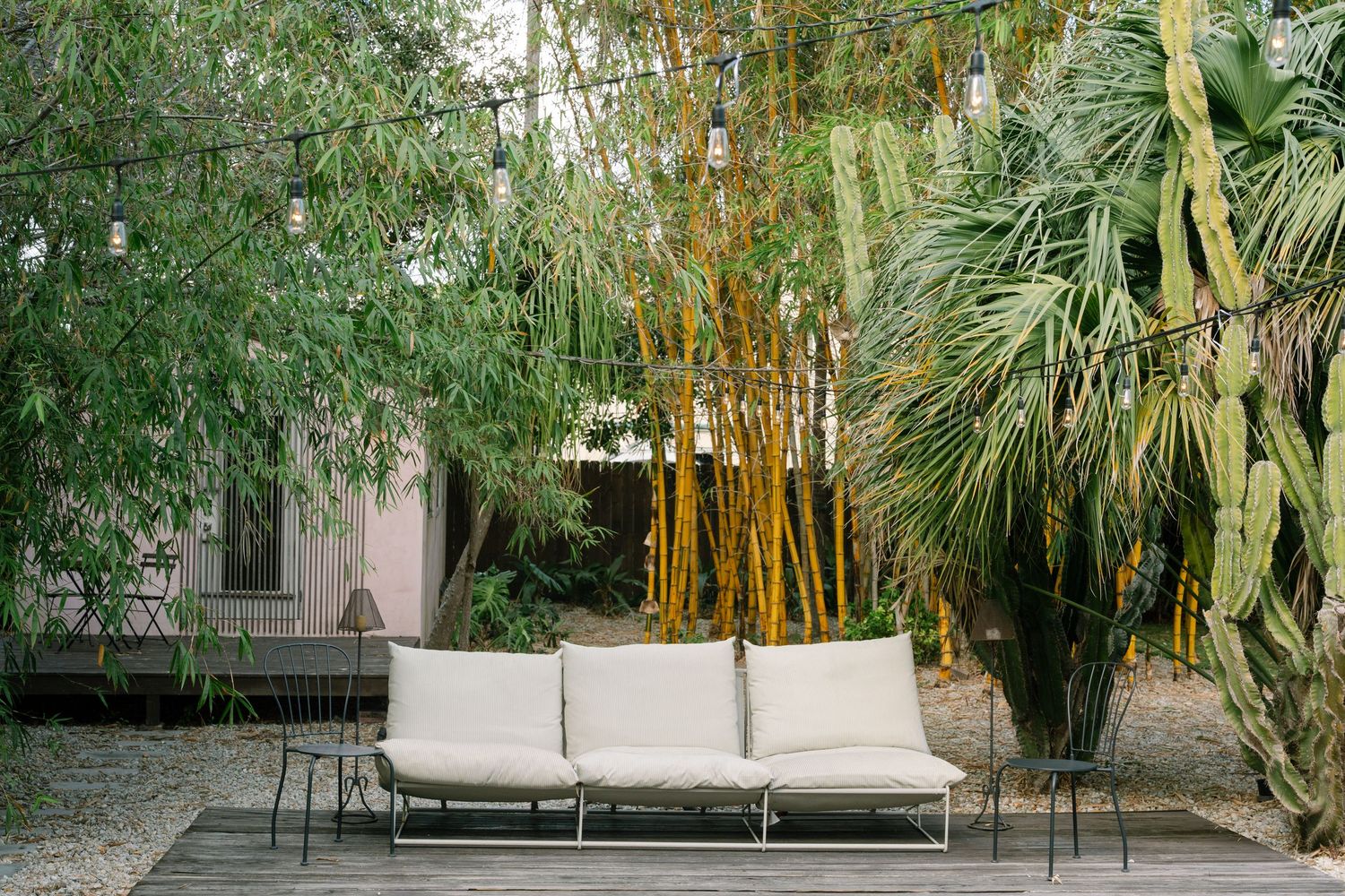 Outdoor lounge area with white furniture surrounded by lush bamboo and tropical plants.