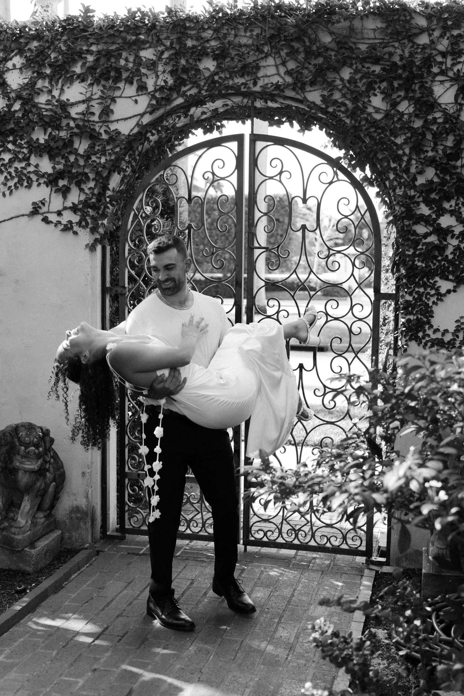 Black and white sequence of guests entering through an ornate garden gate.