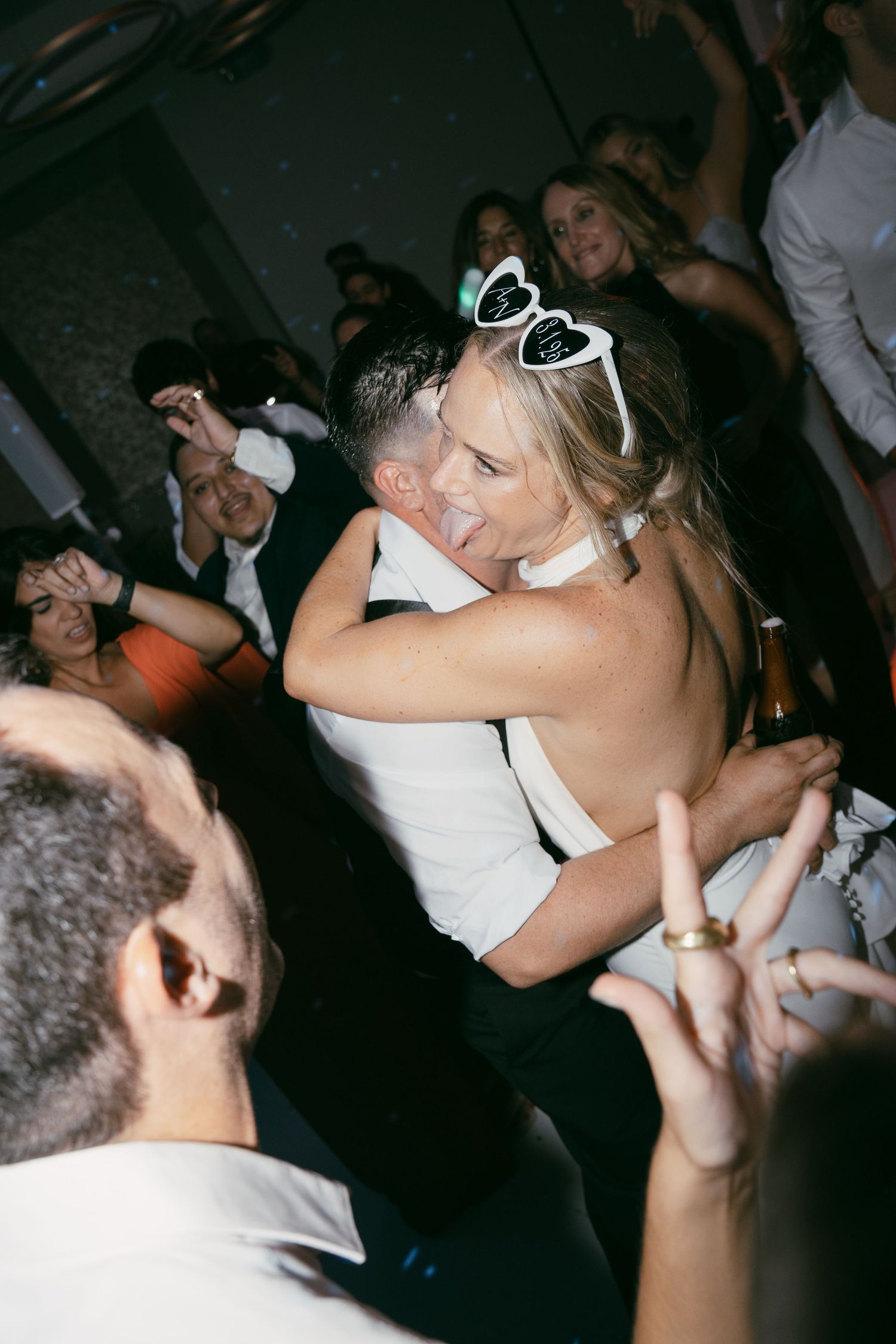 People dancing and celebrating at a lively party with heart-shaped sunglasses and drinks.