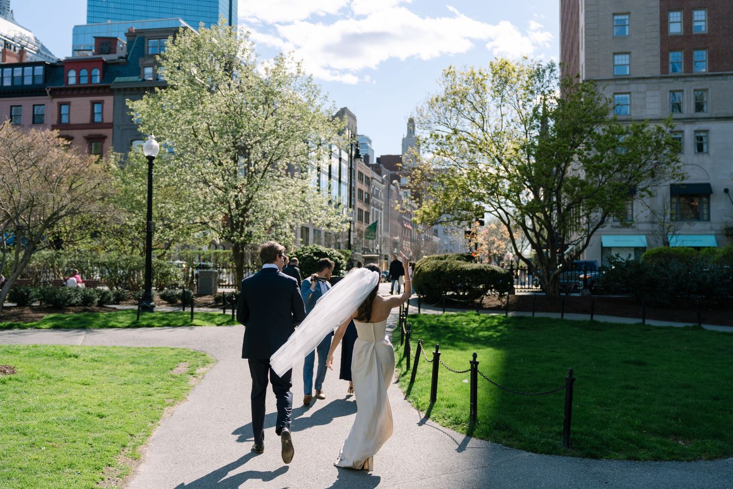 Bride and groom walking through Boston Public Garden on their wedding day with blooming spring trees.
