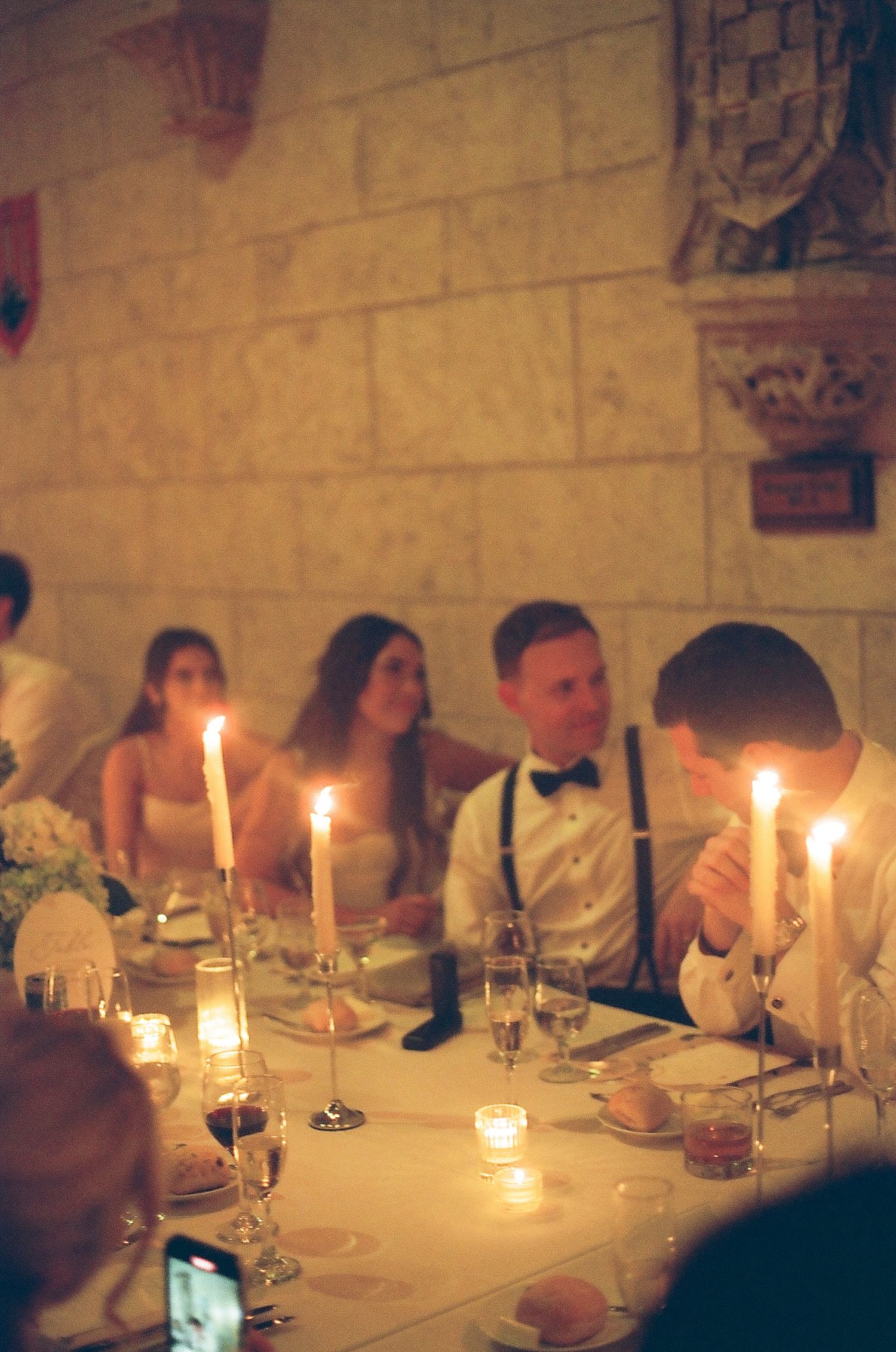Wedding guests seated at candlelit reception dinner table in elegant stone venue.