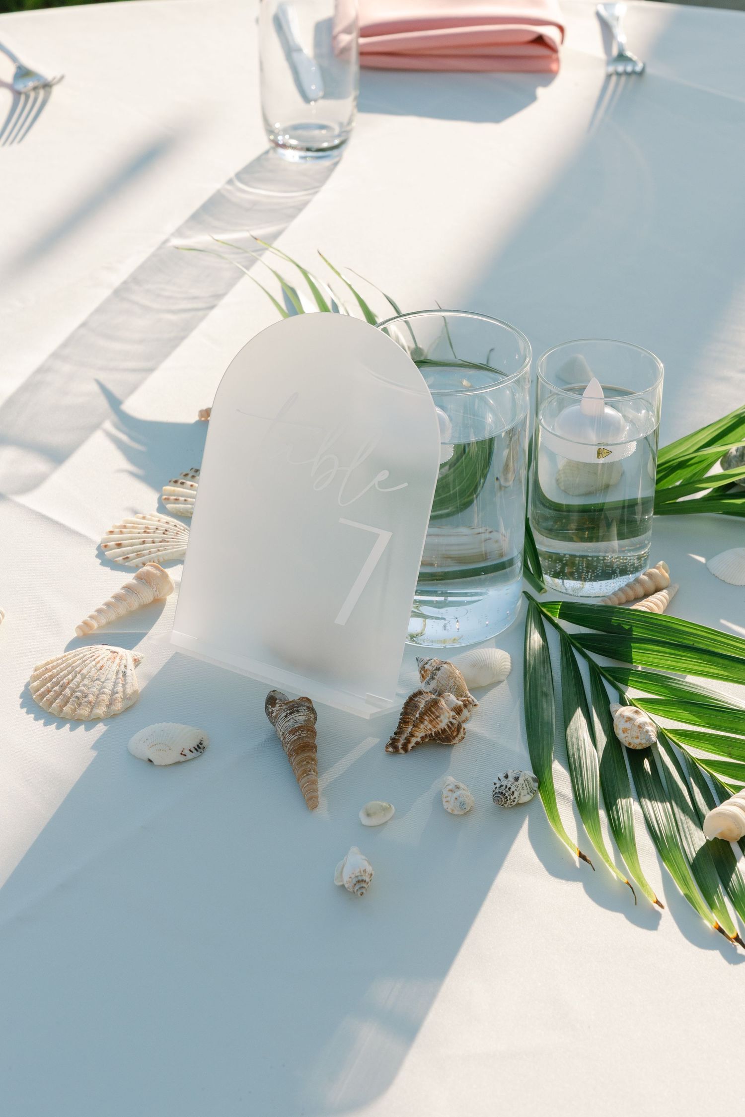 Minimalist beach wedding table decor with seashells, palm leaves and glassware.