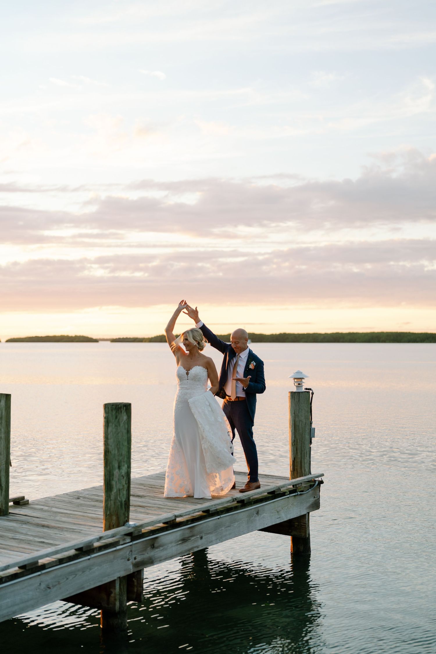 Wedding couple posing on a wooden pier at sunset over tropical waters.
