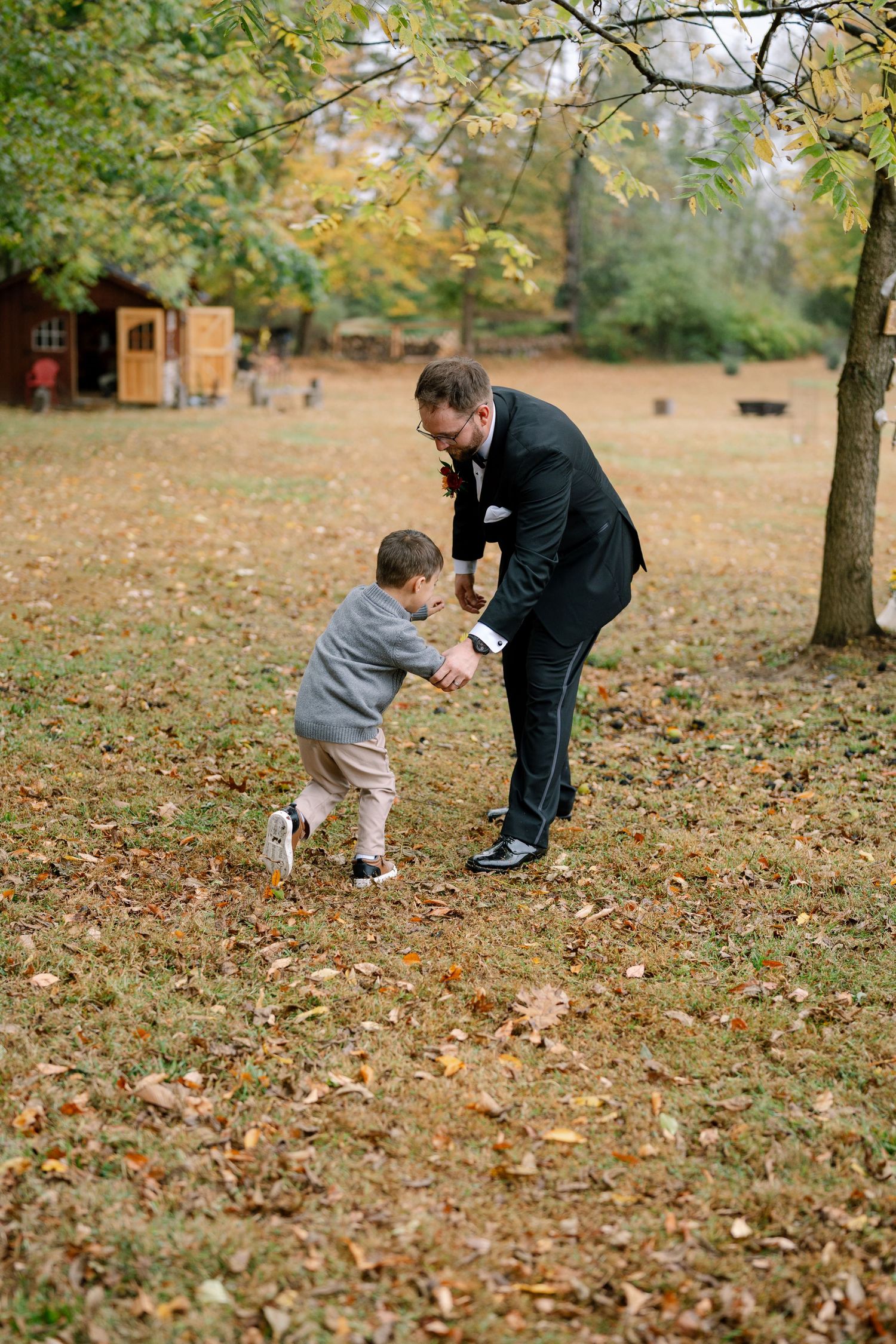 Parent and child playing together in a park covered with fallen autumn leaves on a crisp fall day.
