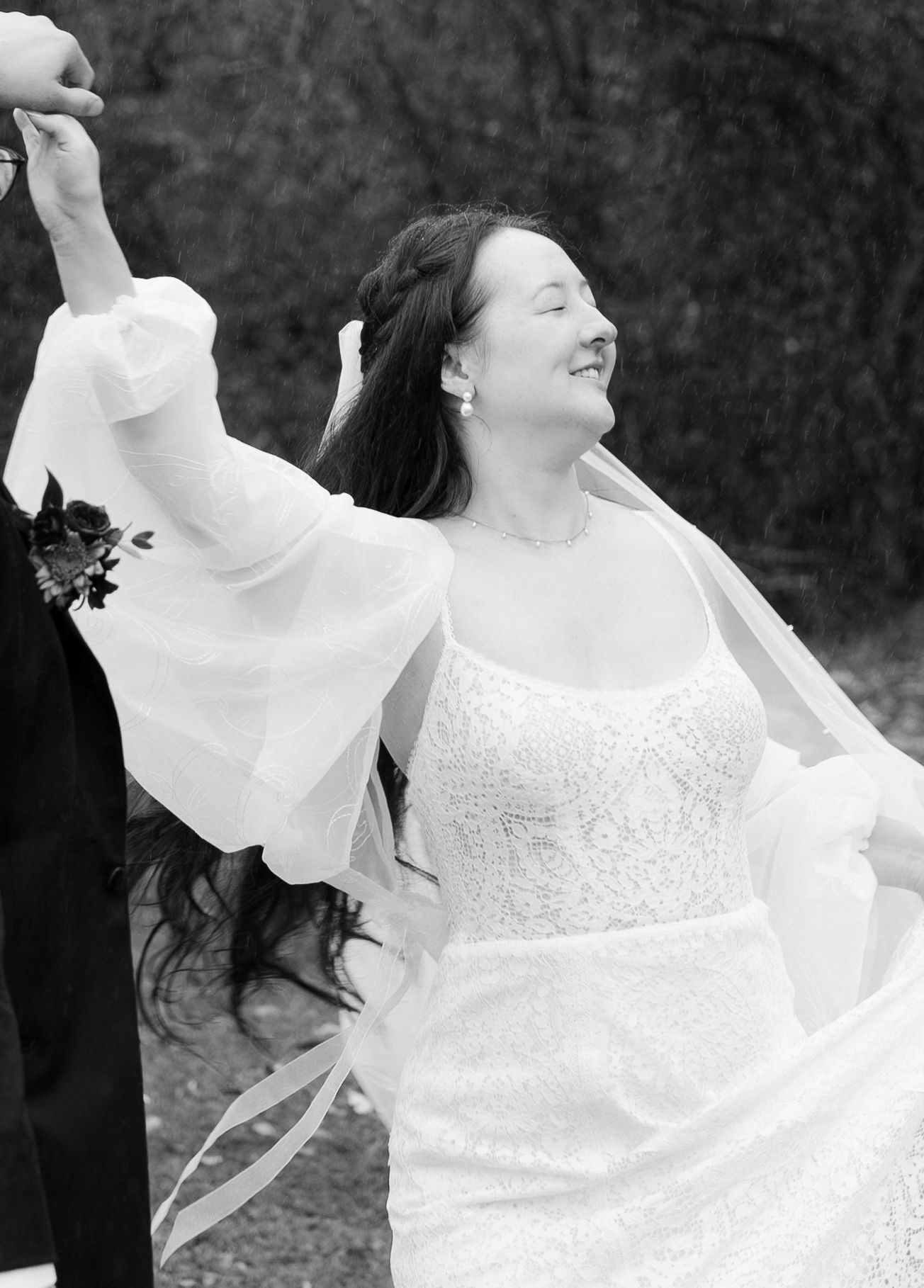 Woman in white lace dress twirling joyfully outdoors in black and white photography.