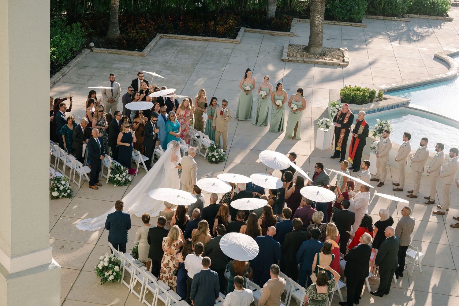 Wedding guests gather in an elegant venue with white columns and natural lighting during a formal celebration.