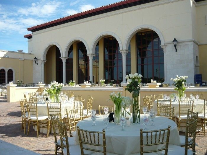 Elegant outdoor wedding reception venue with white tablecloths and gold chiavari chairs under Mediterranean-style arches.