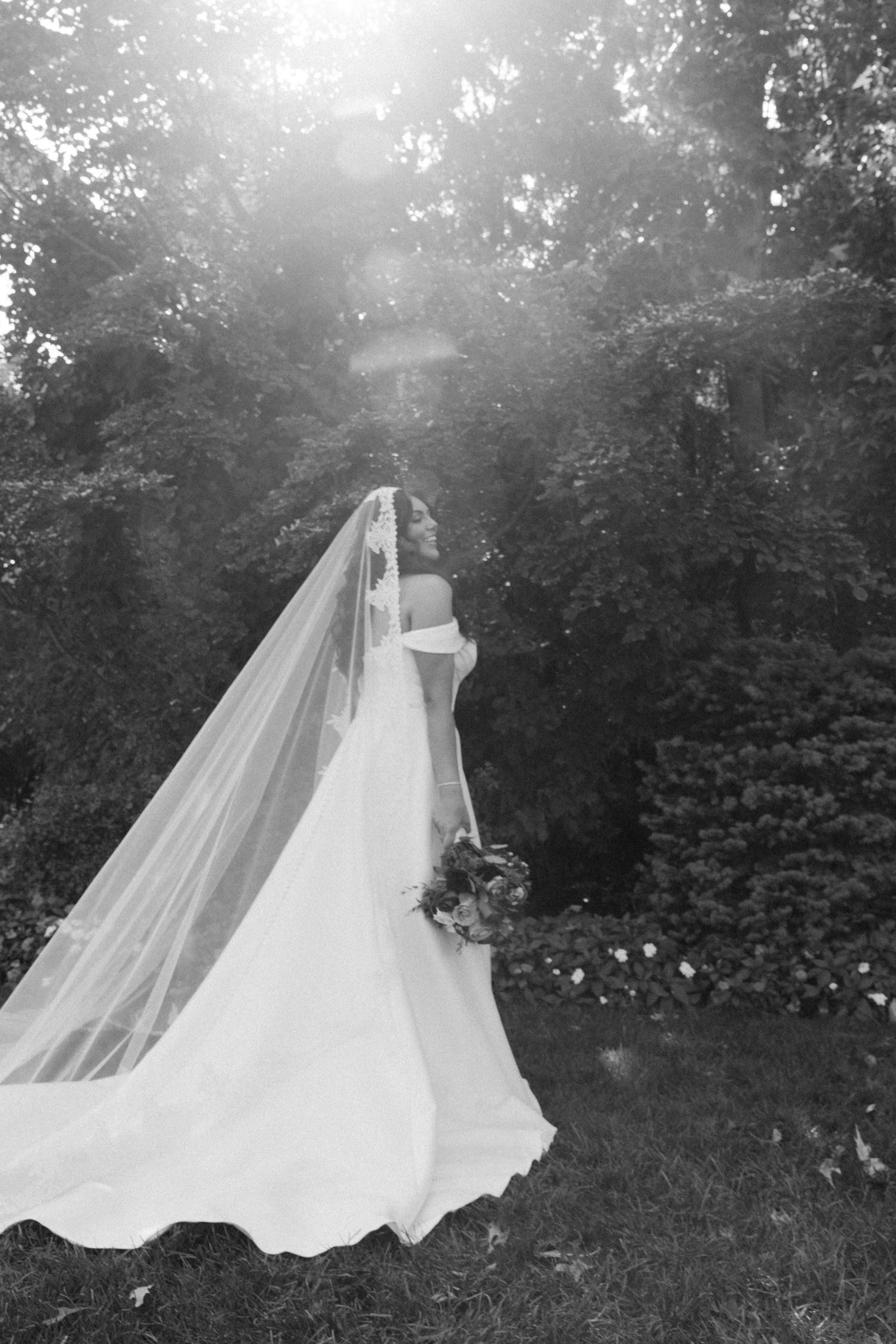Wedding dress with flowing train laid out on grass in dreamy outdoor setting.