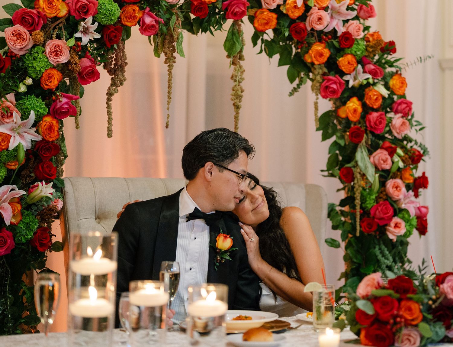 A romantic moment under a vibrant floral arch with red and orange blooms.