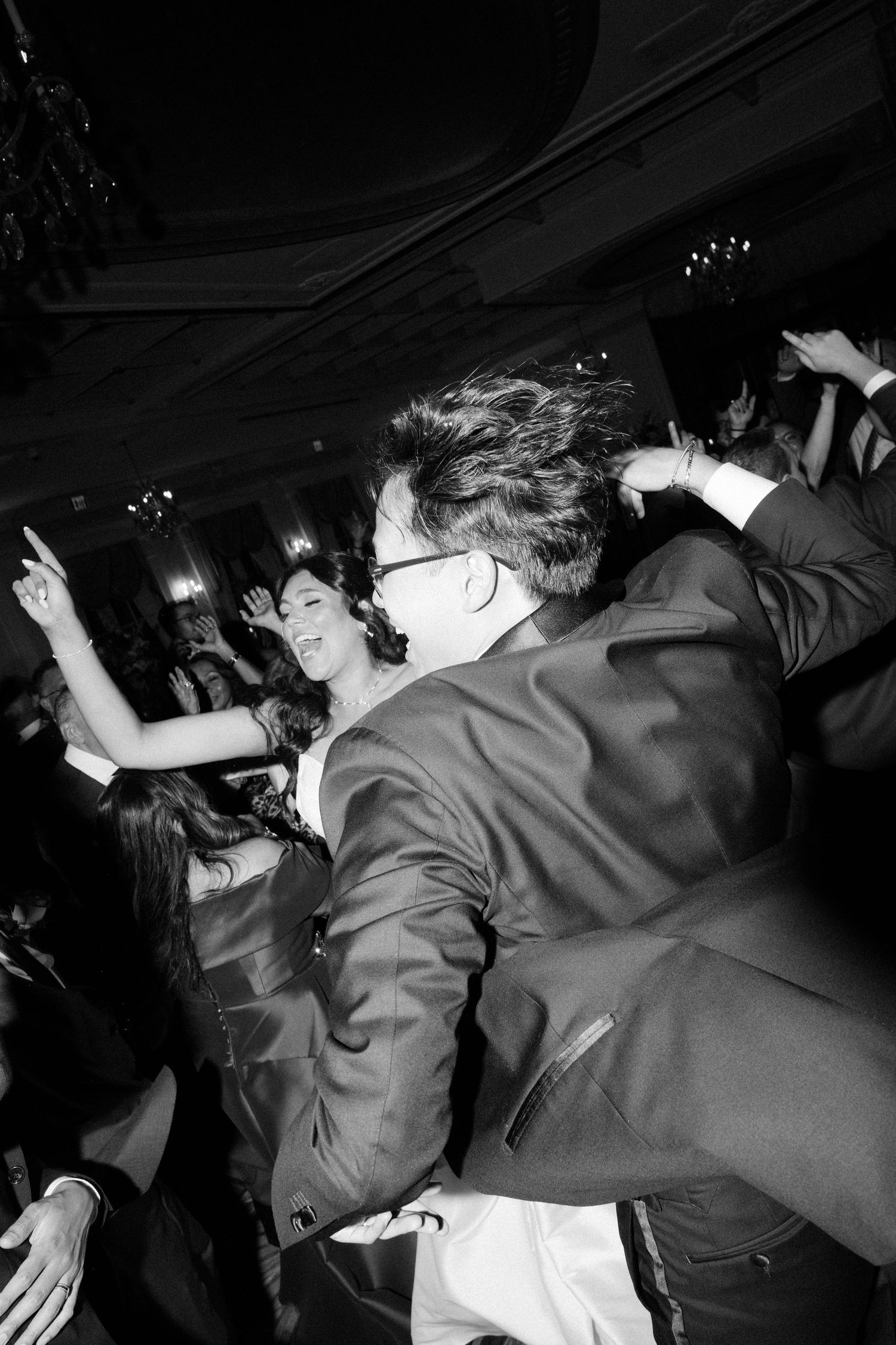 Wedding guests dancing energetically on the dance floor at a reception celebration in black and white.