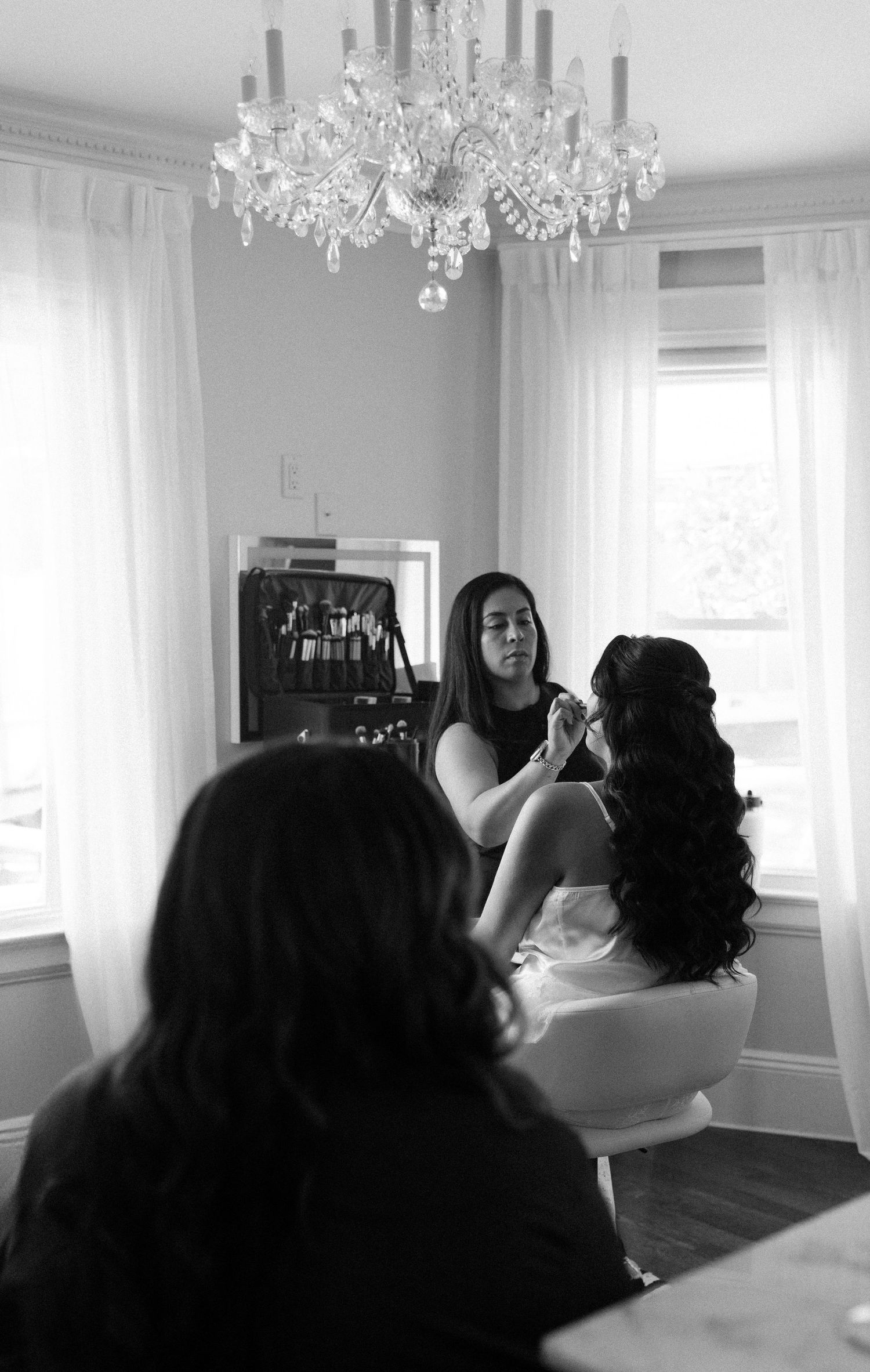 A crystal chandelier hangs above as wedding preparations take place in an elegant room.