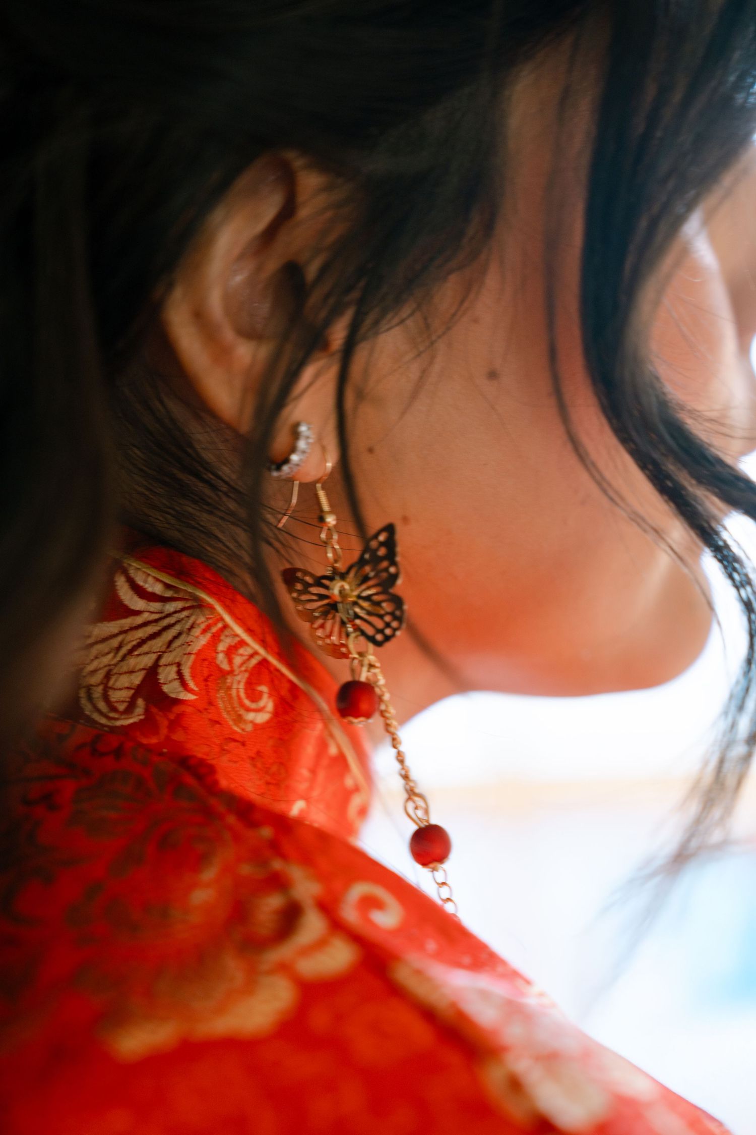 Close-up detail shot of ornate gold butterfly earrings with red lighting effects.