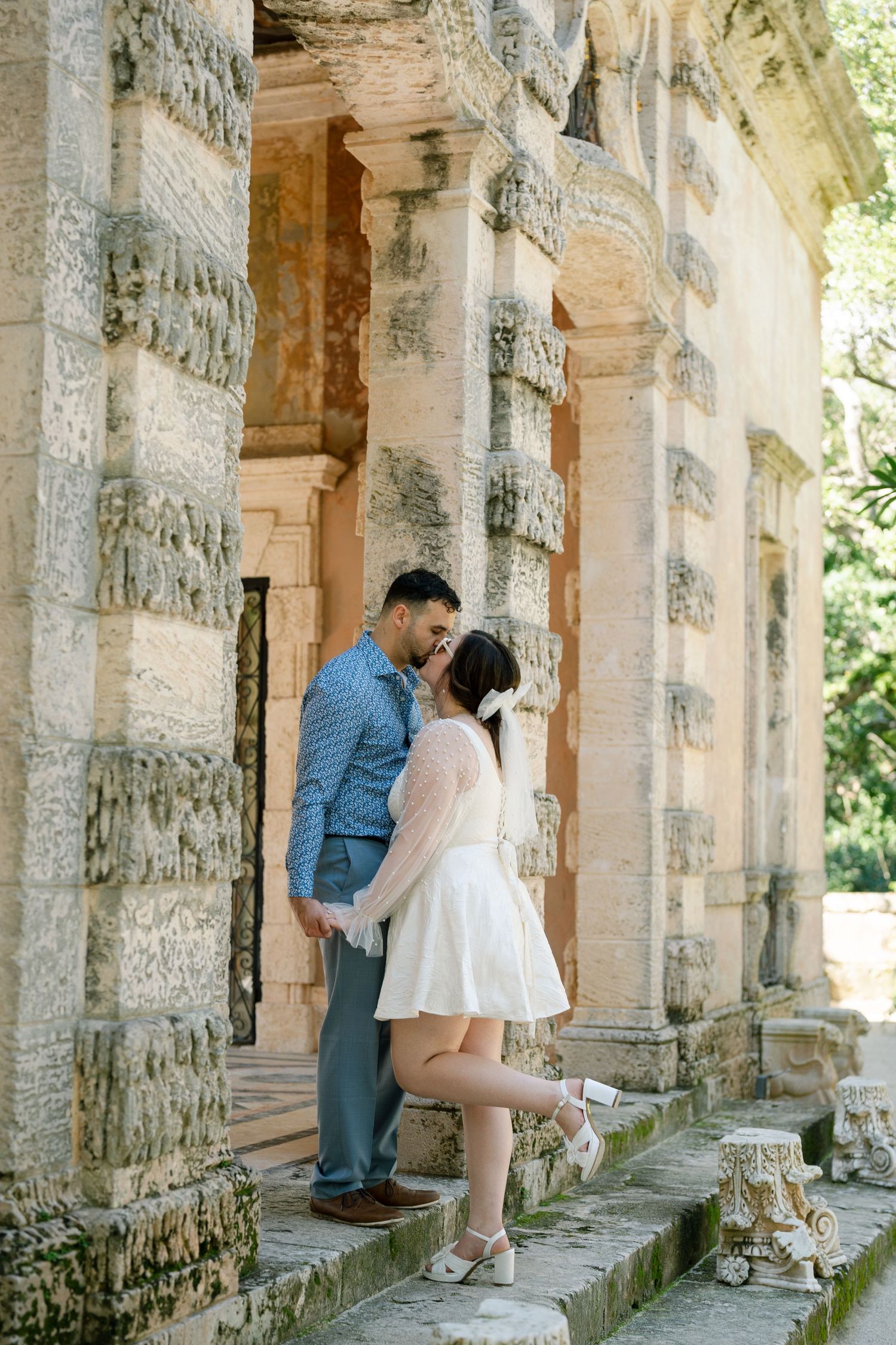 A couple sharing an intimate moment among stone pillars in a classical architectural setting.