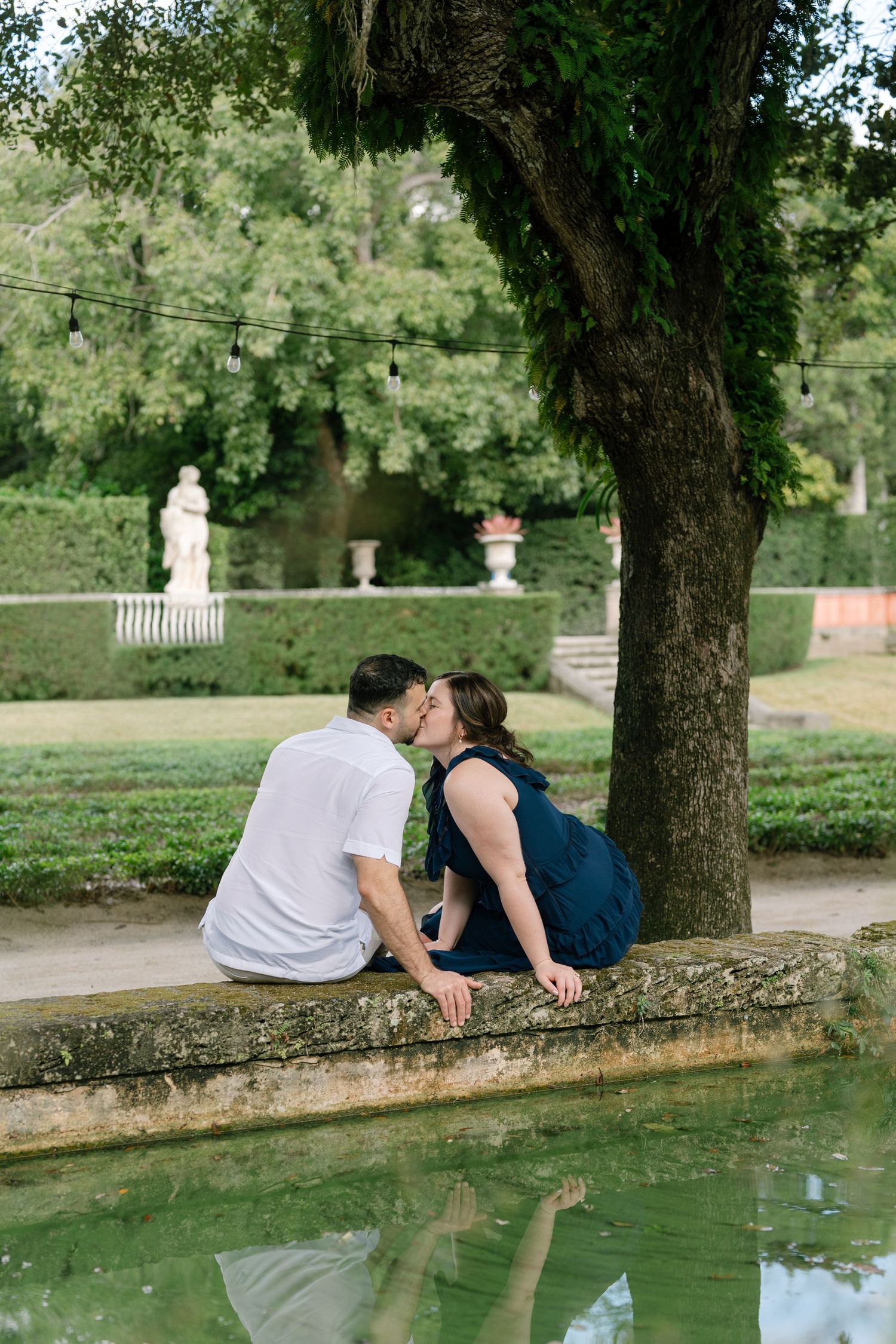 Couple sitting on stone wall beside reflecting pool in garden setting.