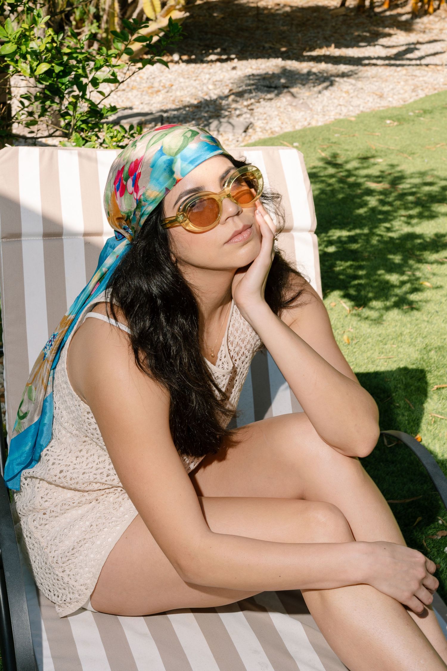 Woman in white top and blue head scarf relaxing outdoors on a sunny day.