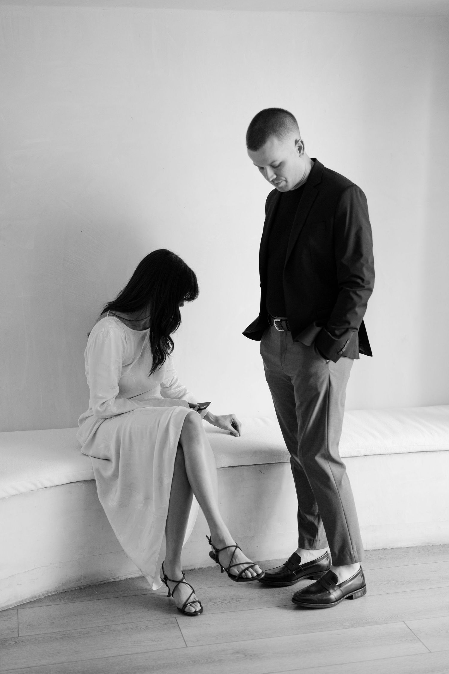 Black and white sequence showing two people sitting against a white wall in various poses.