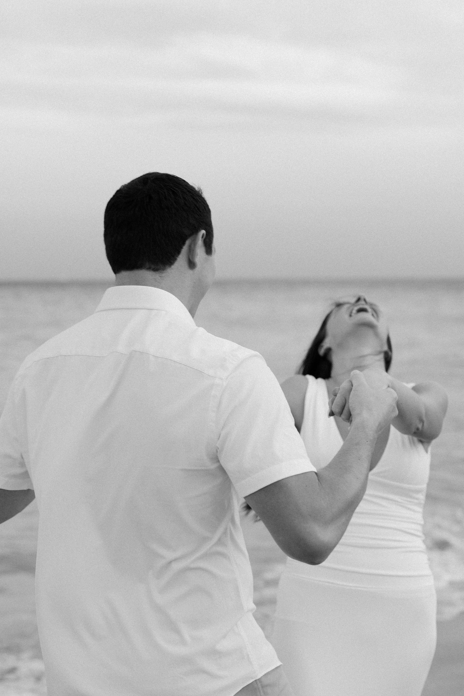 A couple in white clothing taking photos together on a beach during an overcast day.