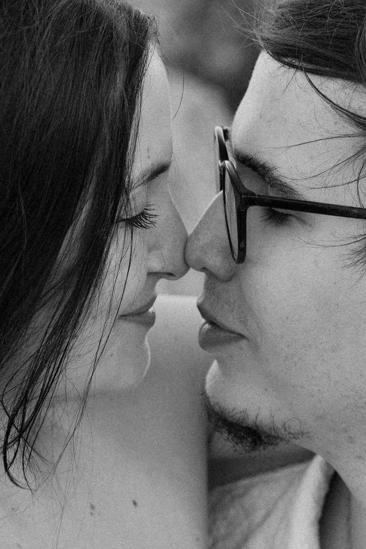 A romantic black and white close-up photograph of a couple about to kiss, with one person wearing glasses.