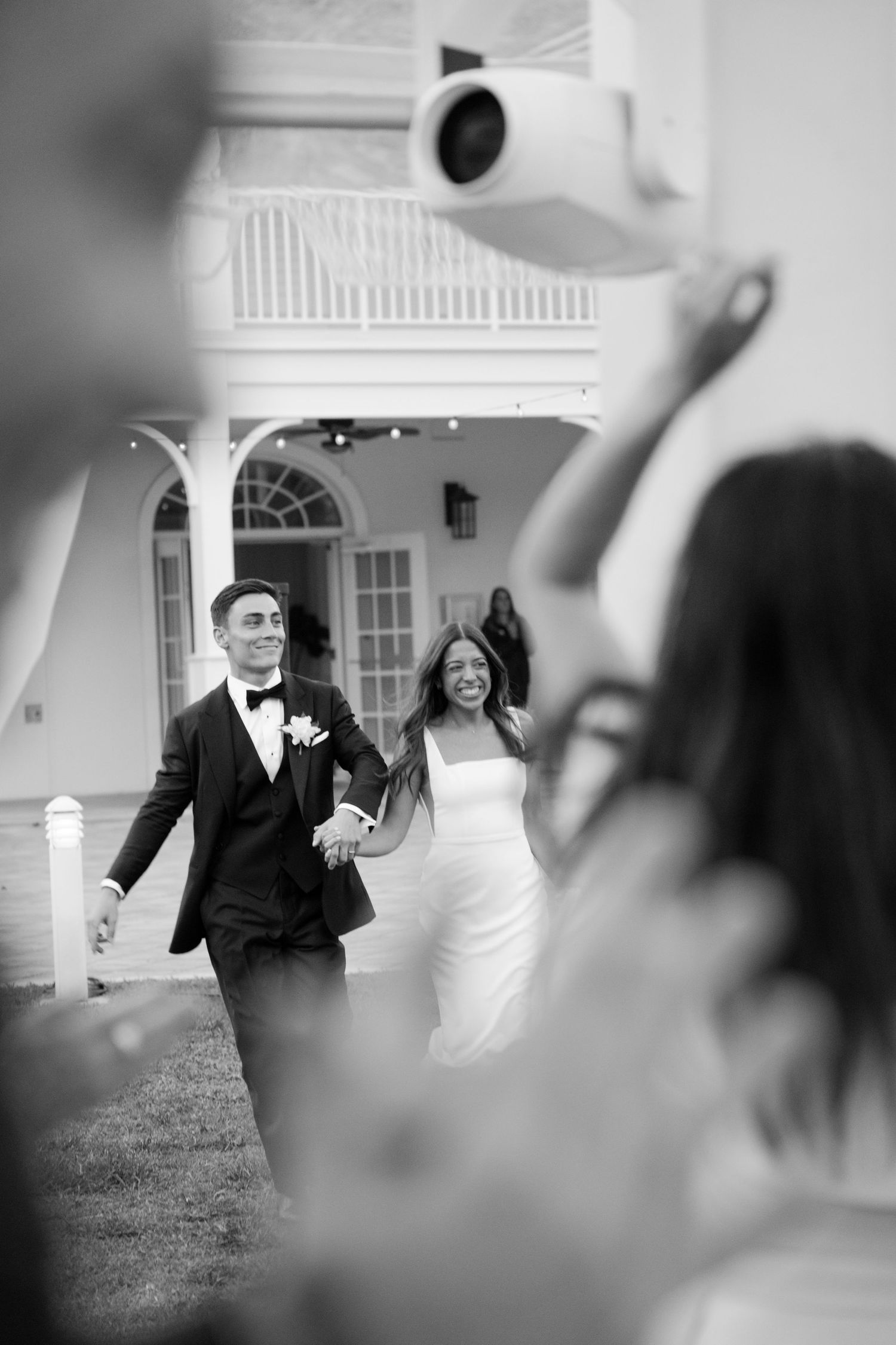 Bride and groom walking hand in hand toward cheering guests at their wedding reception.