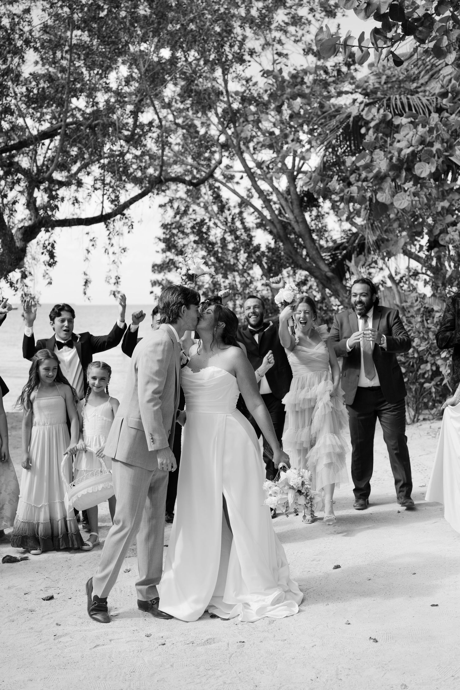 A group of people, including a bride and groom, walking together in an outdoor setting with trees and foliage.